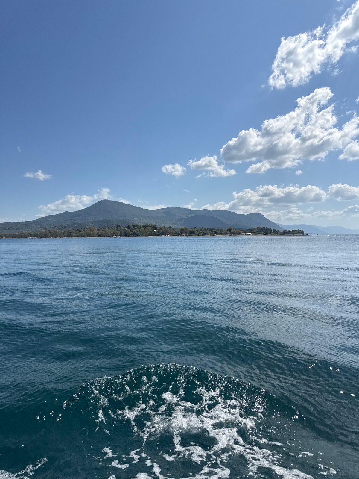 Boat cuts through calm Greek waters toward a wooded island