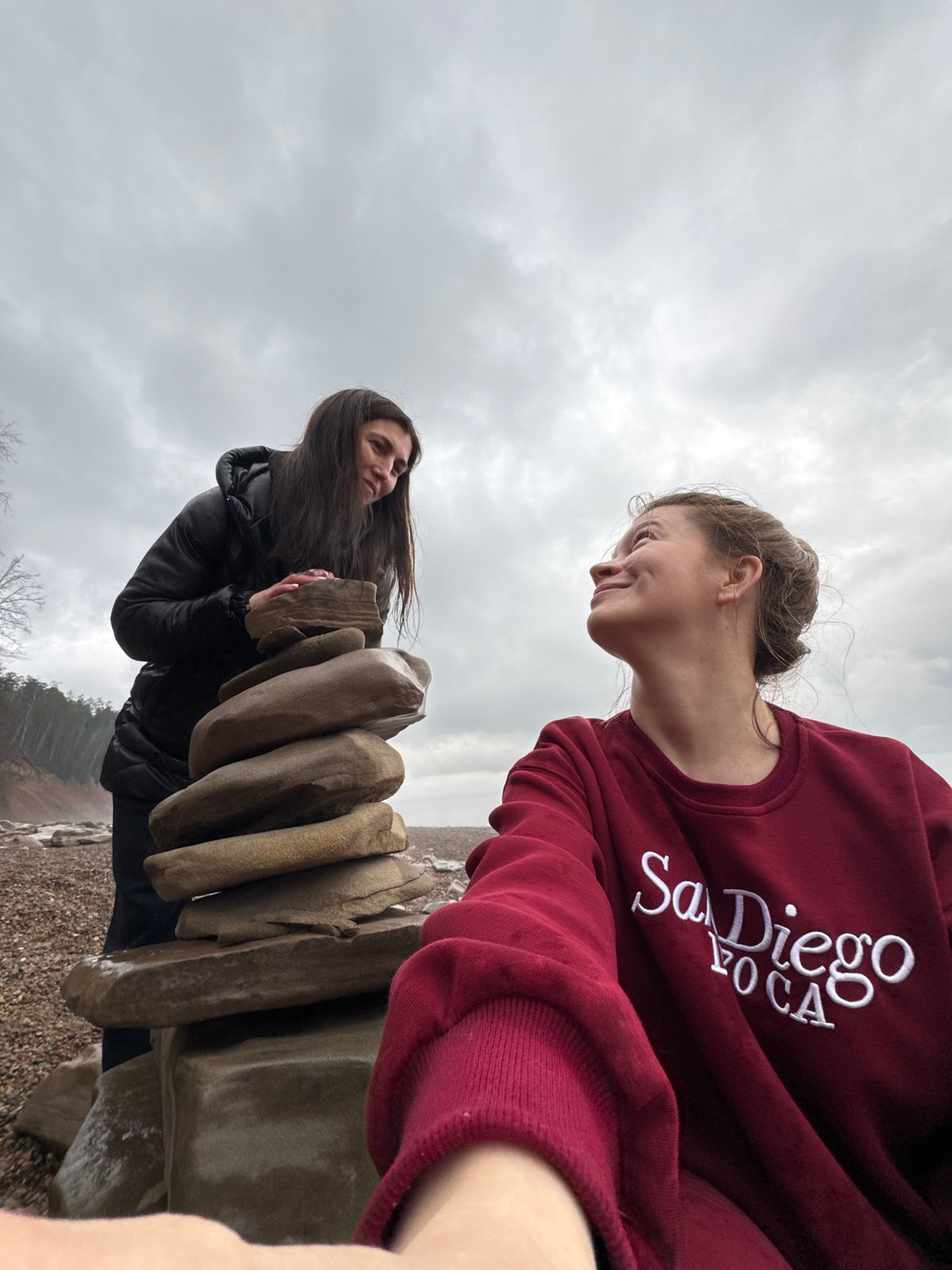Two women gather near stacked rocks by waterway in Russia