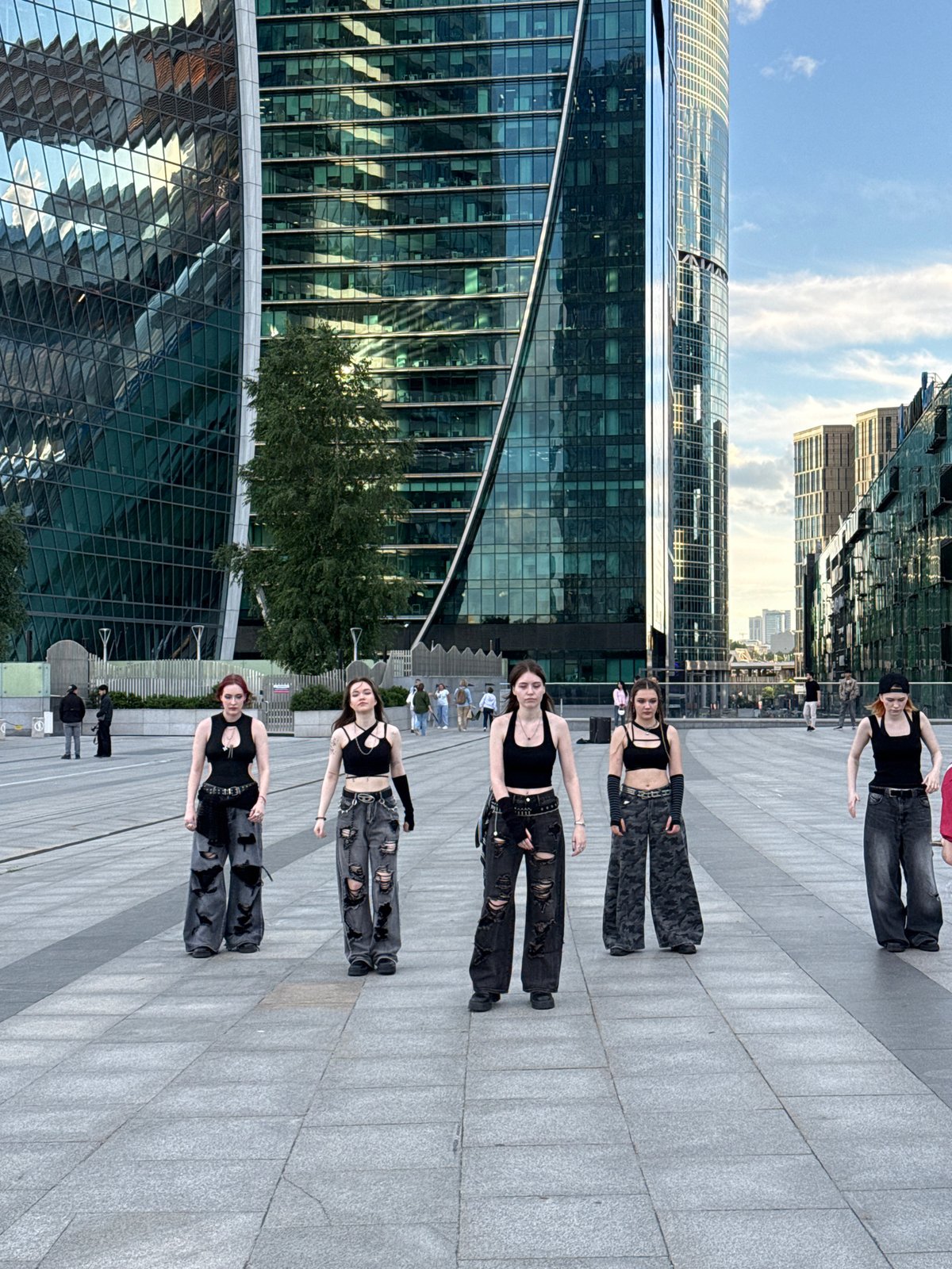 Streetwear crew dancing in a downtown plaza among skyscrapers