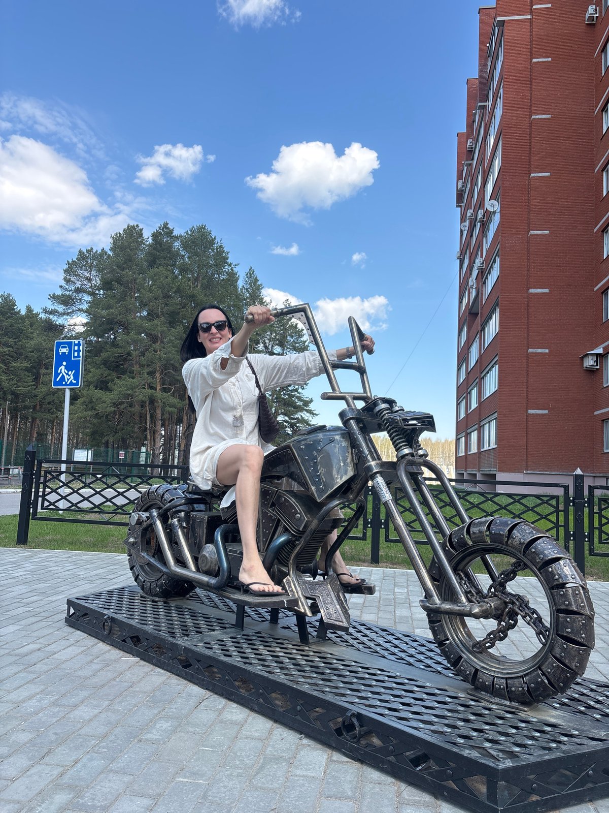 Woman poses with thumbs-up on motorcycle sculpture in Chaikovsky