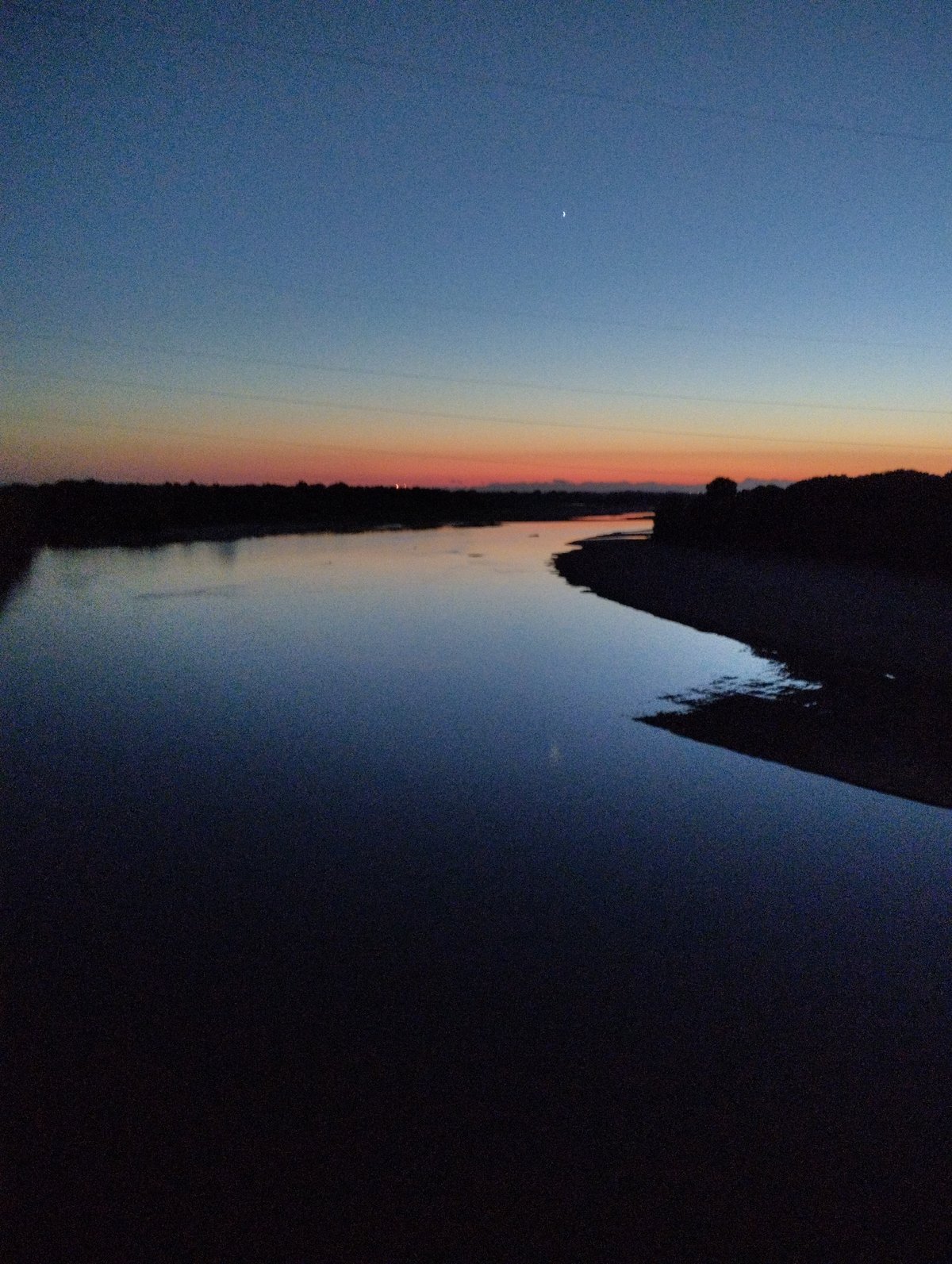 Crane lifts debris from structure near river at dusk