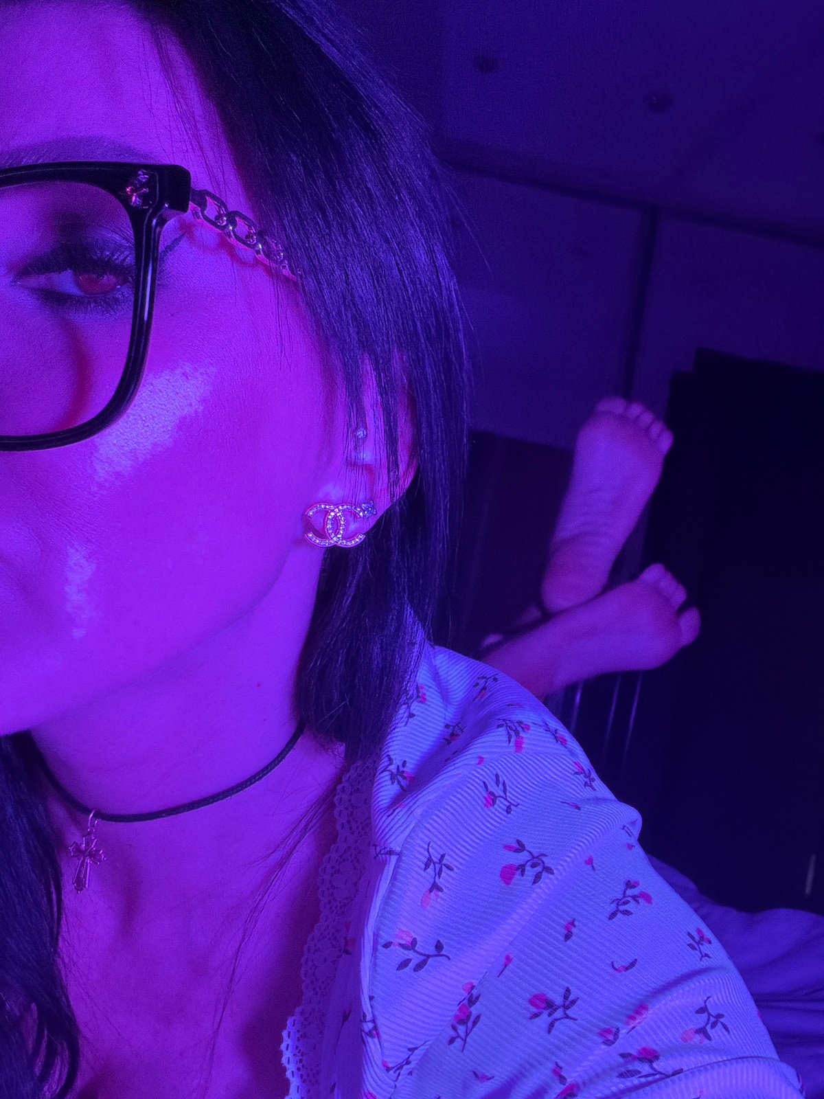 Person photographed in purple light wearing glasses and cross necklace