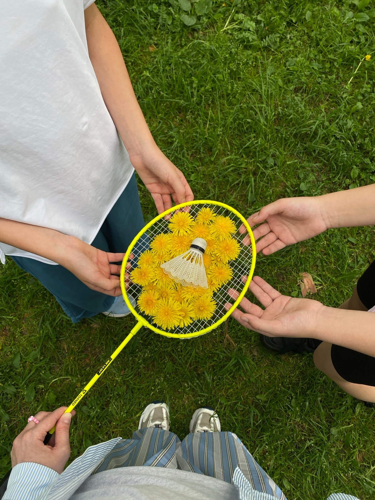 Group plays with dandelion-filled badminton racket outdoors