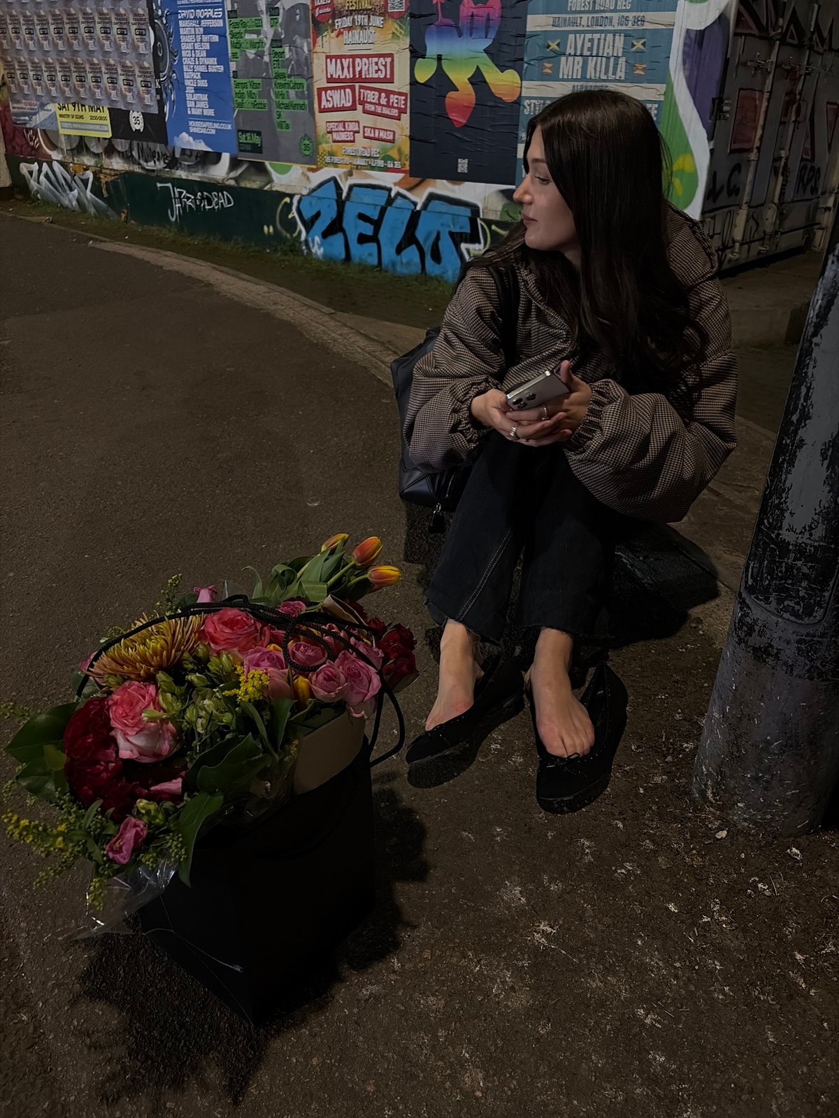 Person sits with flower bouquet beside poster-covered wall in London