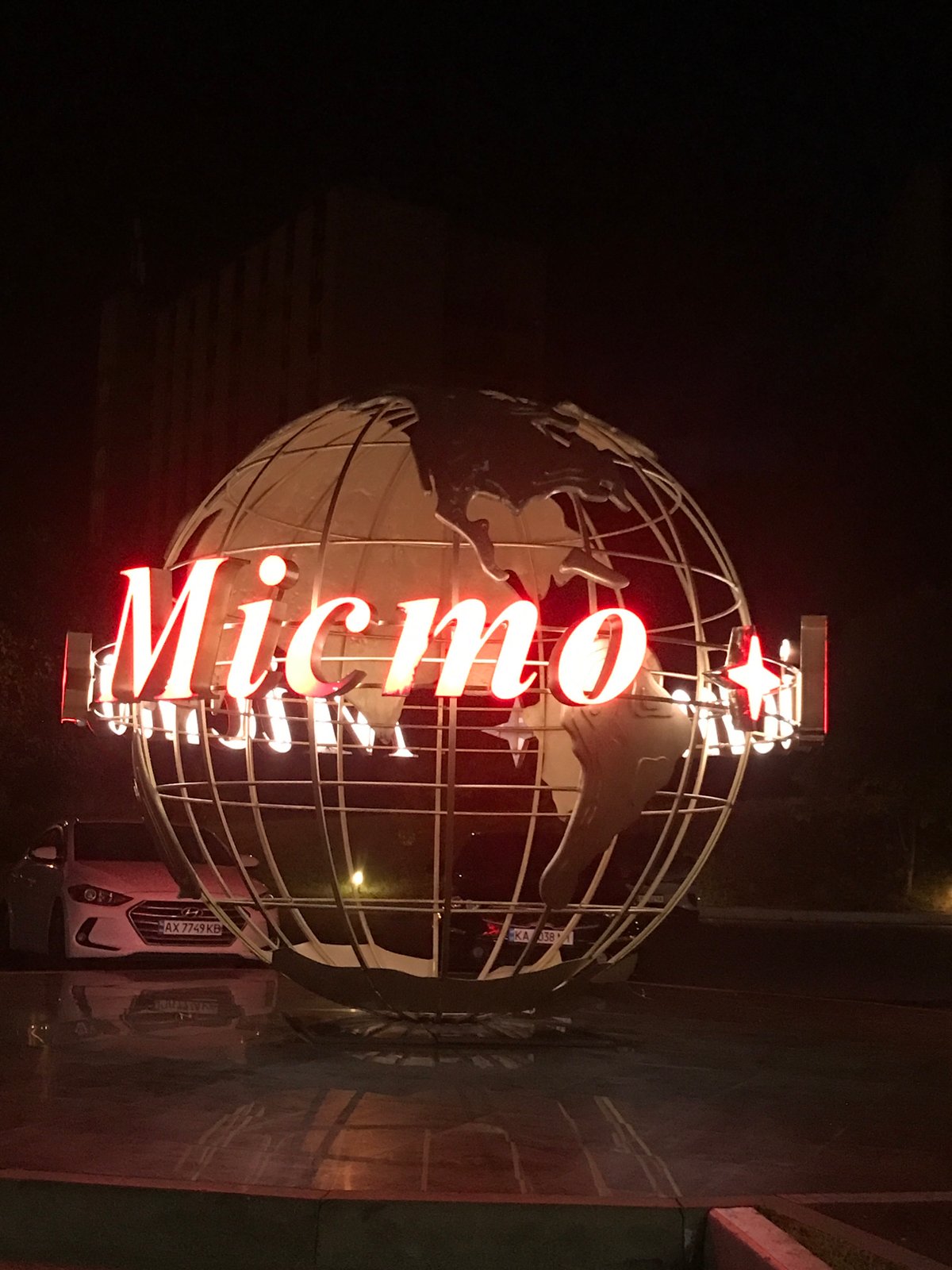 Illuminated wireframe globe sculpture with red neon signage at night