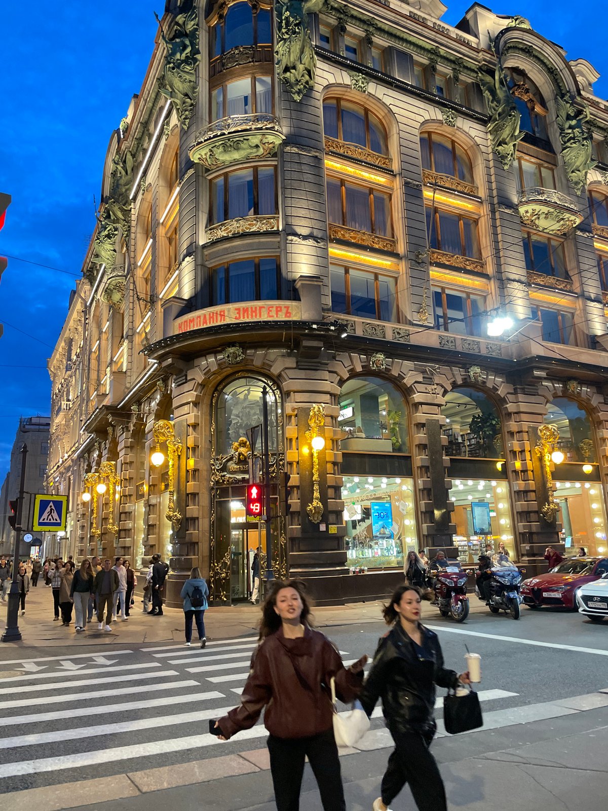Evening street activity outside a lit ornate European building