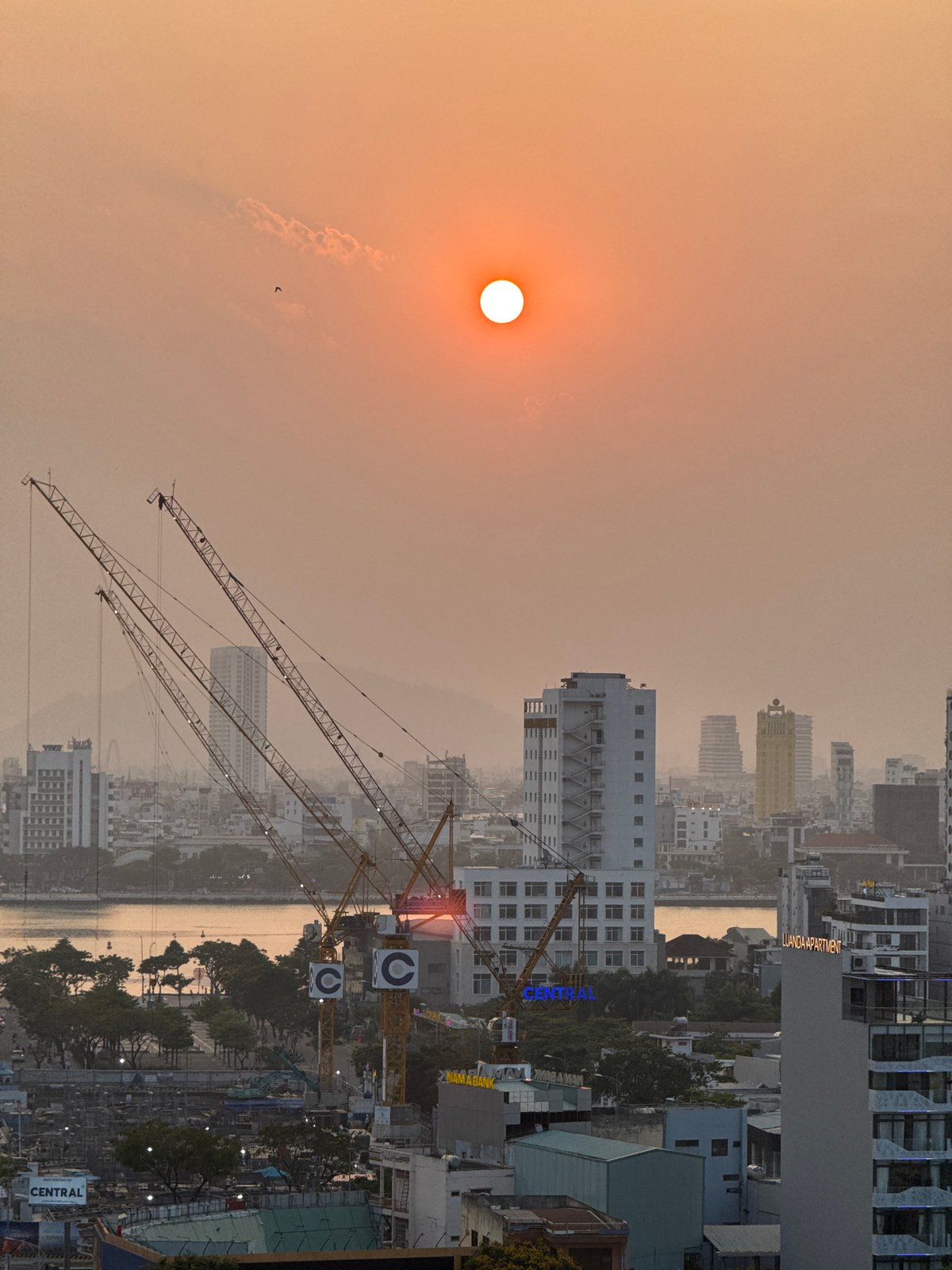 Hazy sunset illuminates construction cranes in Đà Nẵng cityscape