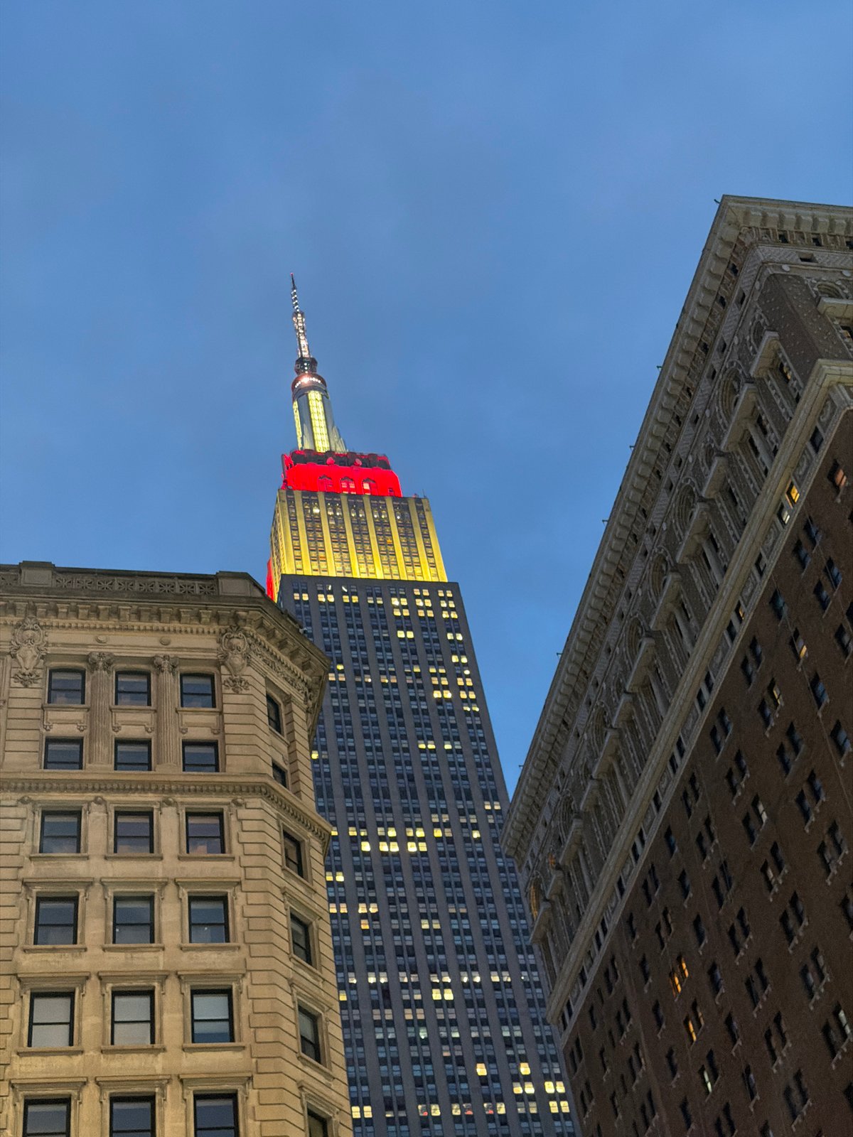 Empire State Building glowing red and yellow on a Midtown night