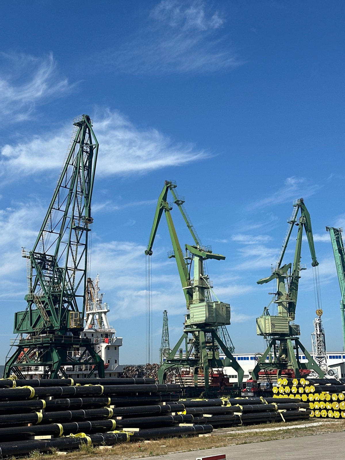 Industrial port waterfront with cranes, pipes, and calm water nearby