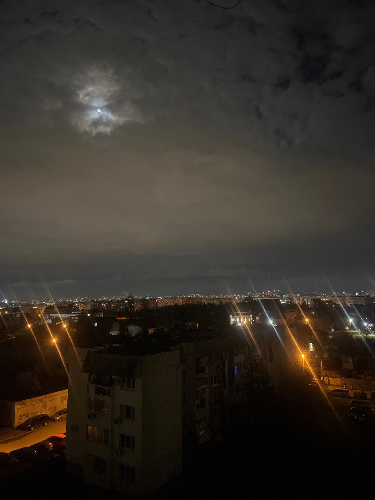 Moon breaks through clouds over Sofia's illuminated nighttime skyline