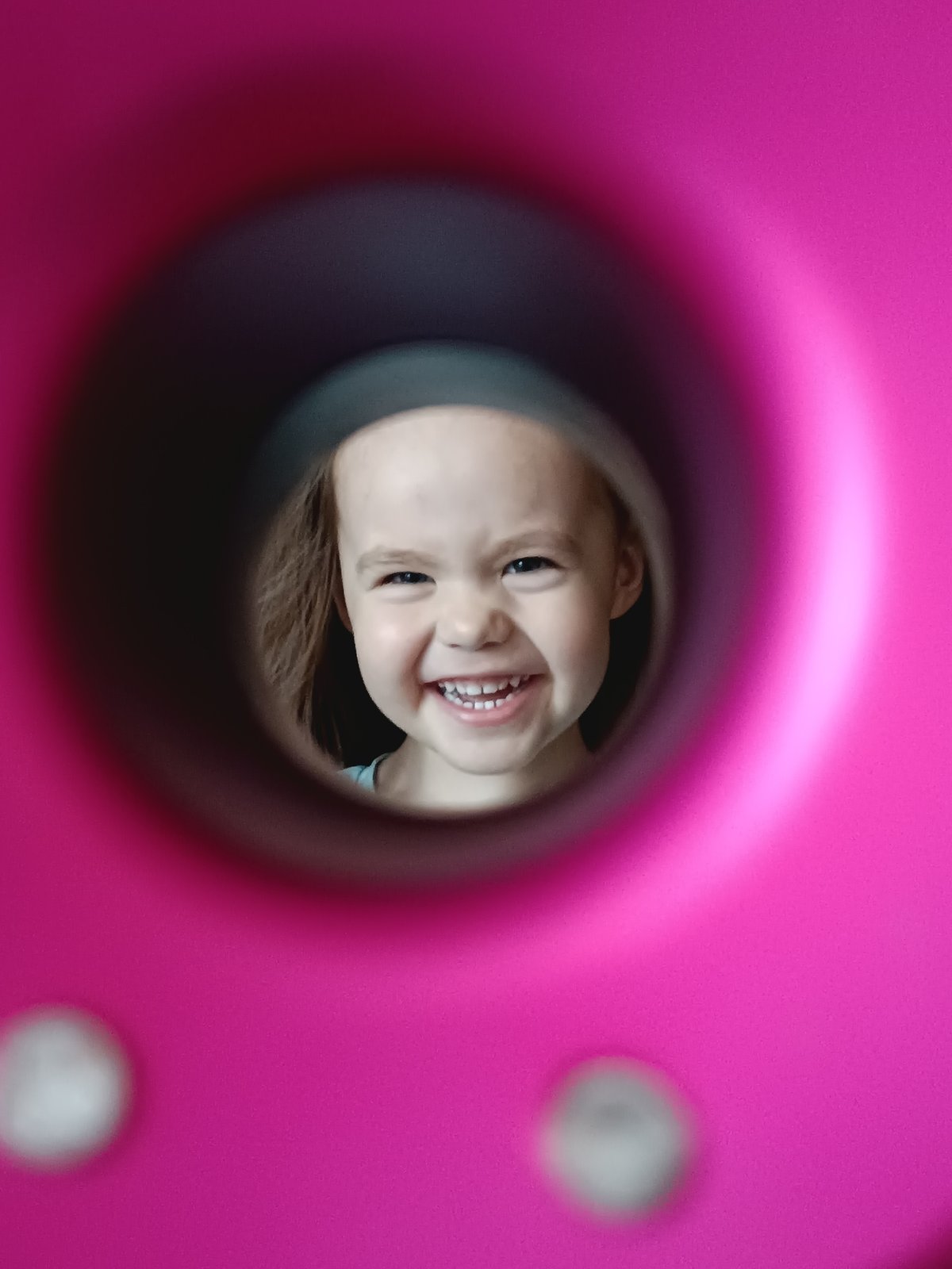 Child plays on playground equipment, smiles through circular openings