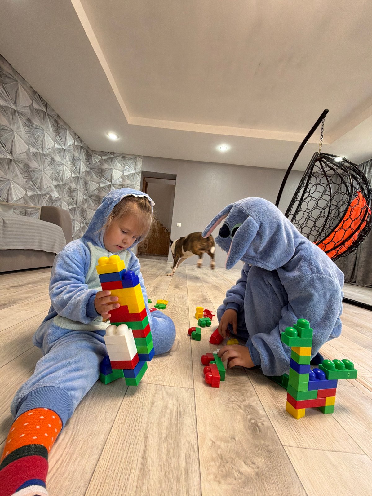 Children in blue onesies play with building blocks indoors