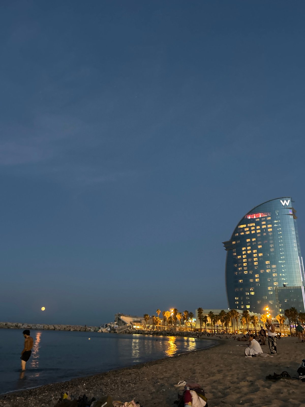 Full moon rises over Barcelona's calm waterfront at twilight