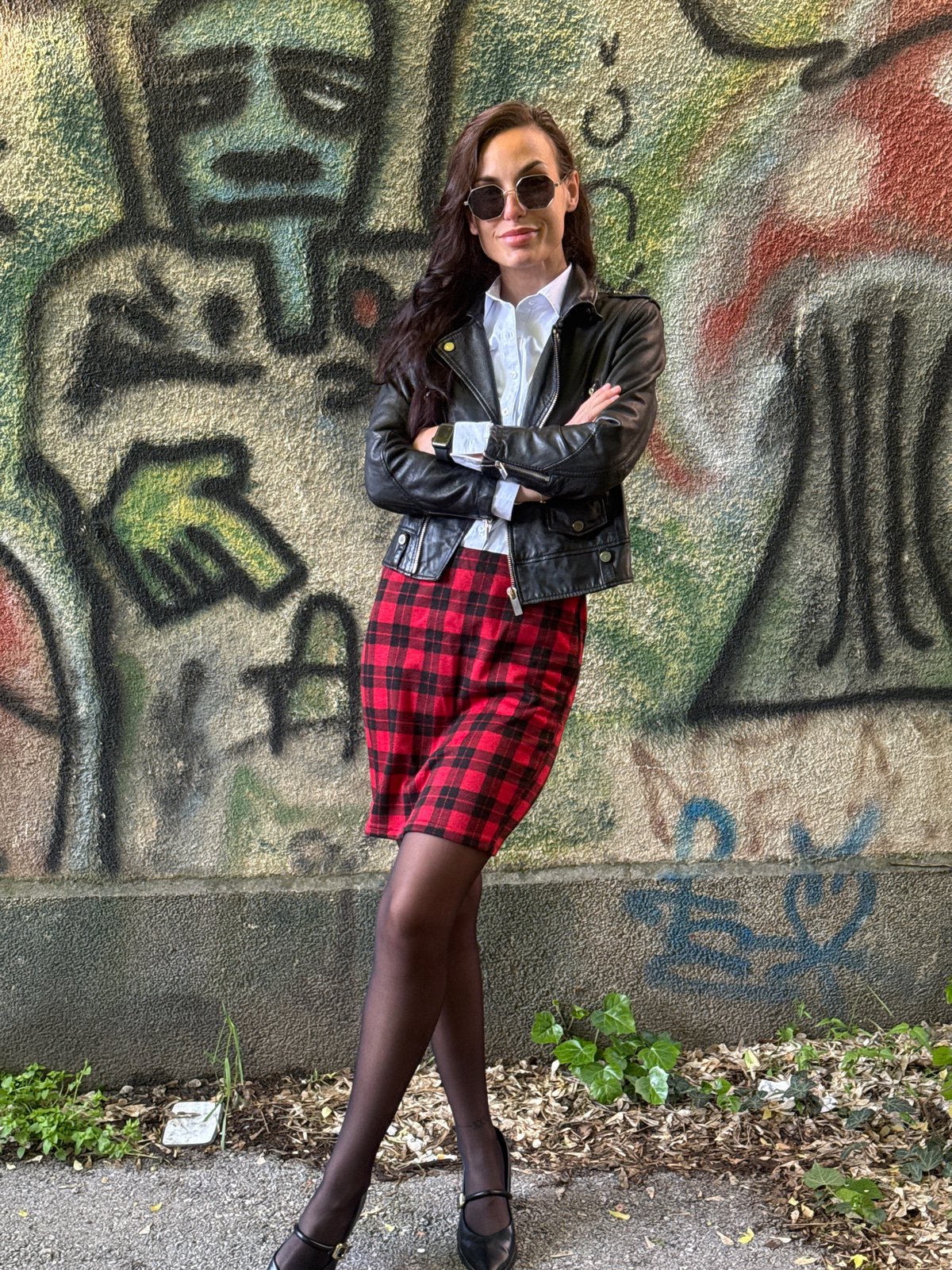 Woman in plaid skirt rests against graffitied wall in Pleven