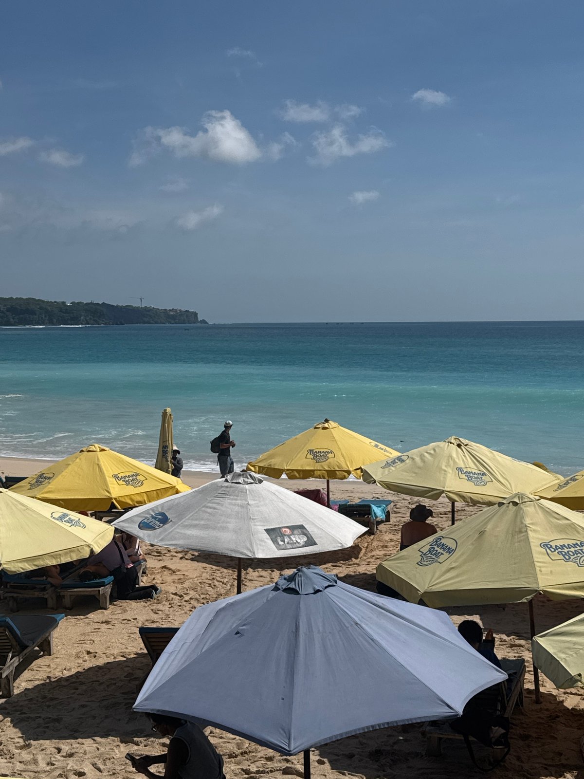 Banana Boat umbrellas shade morning beachgoers in Kuta Selatan