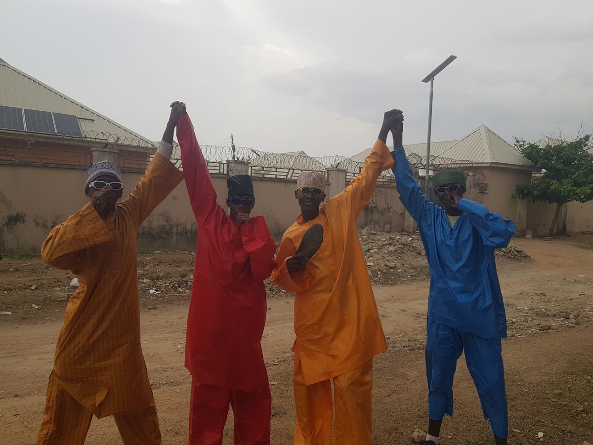 Four robed figures gather, walk dirt path outdoors