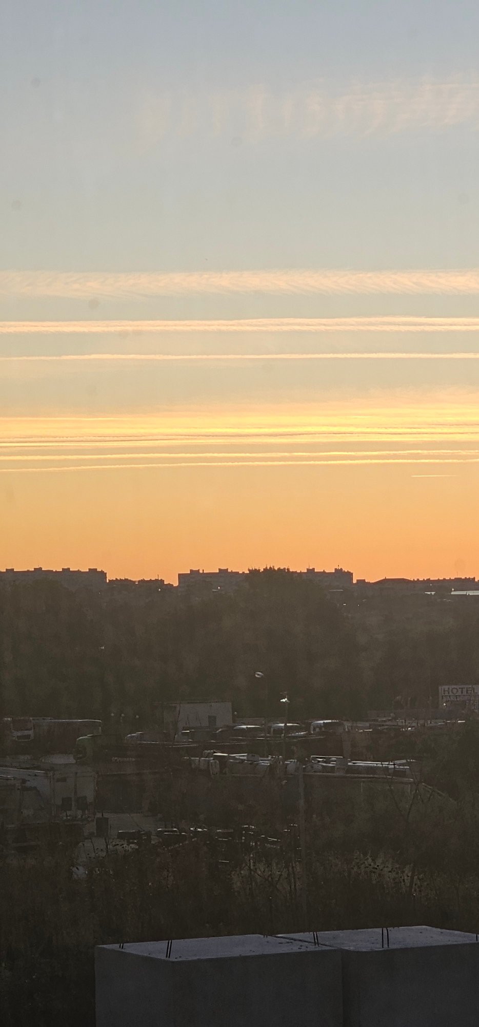 City skyline at dusk, contrails and soft gradients across the sky