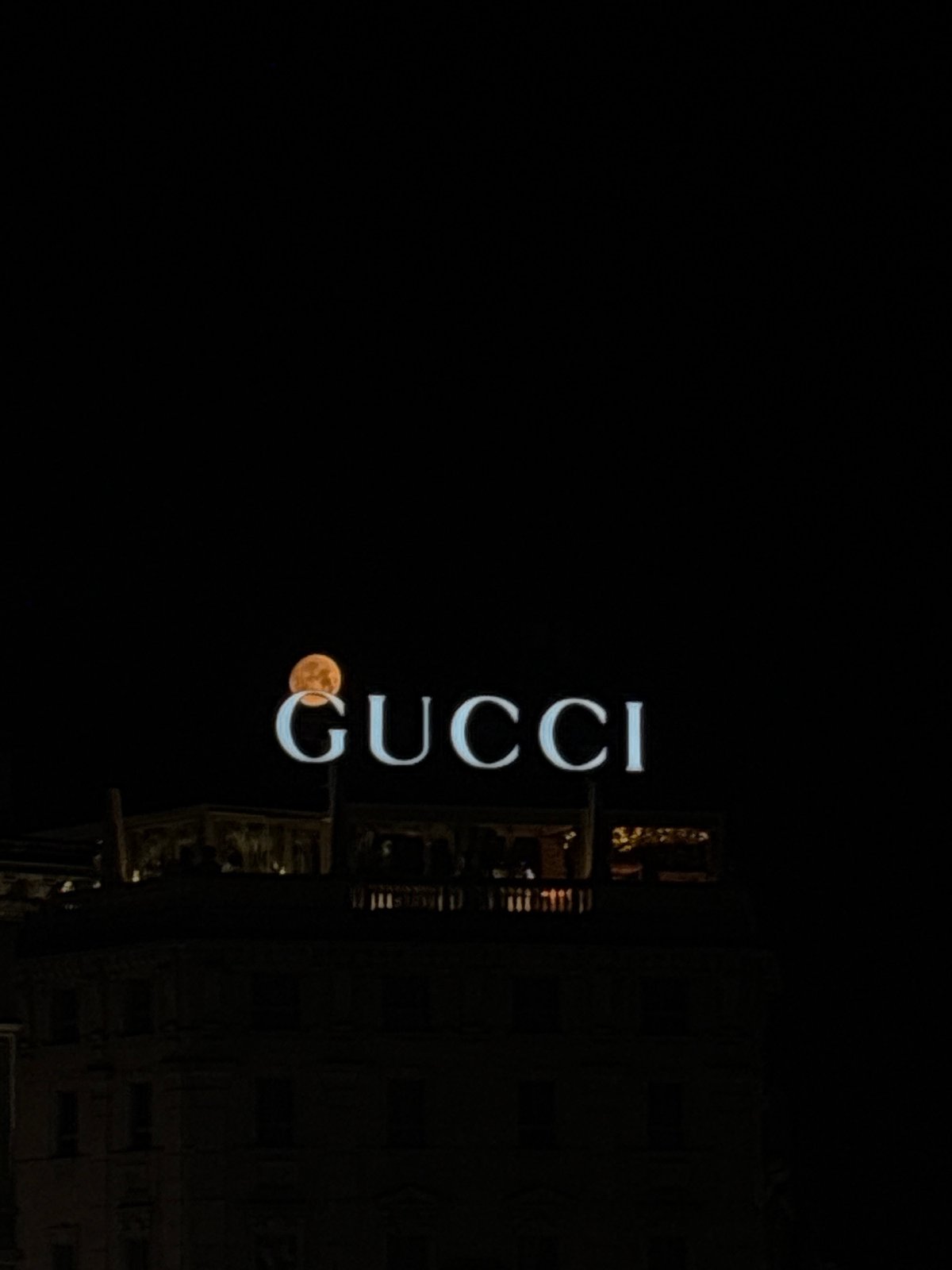 Gucci sign and full orange moon align over Milan night sky