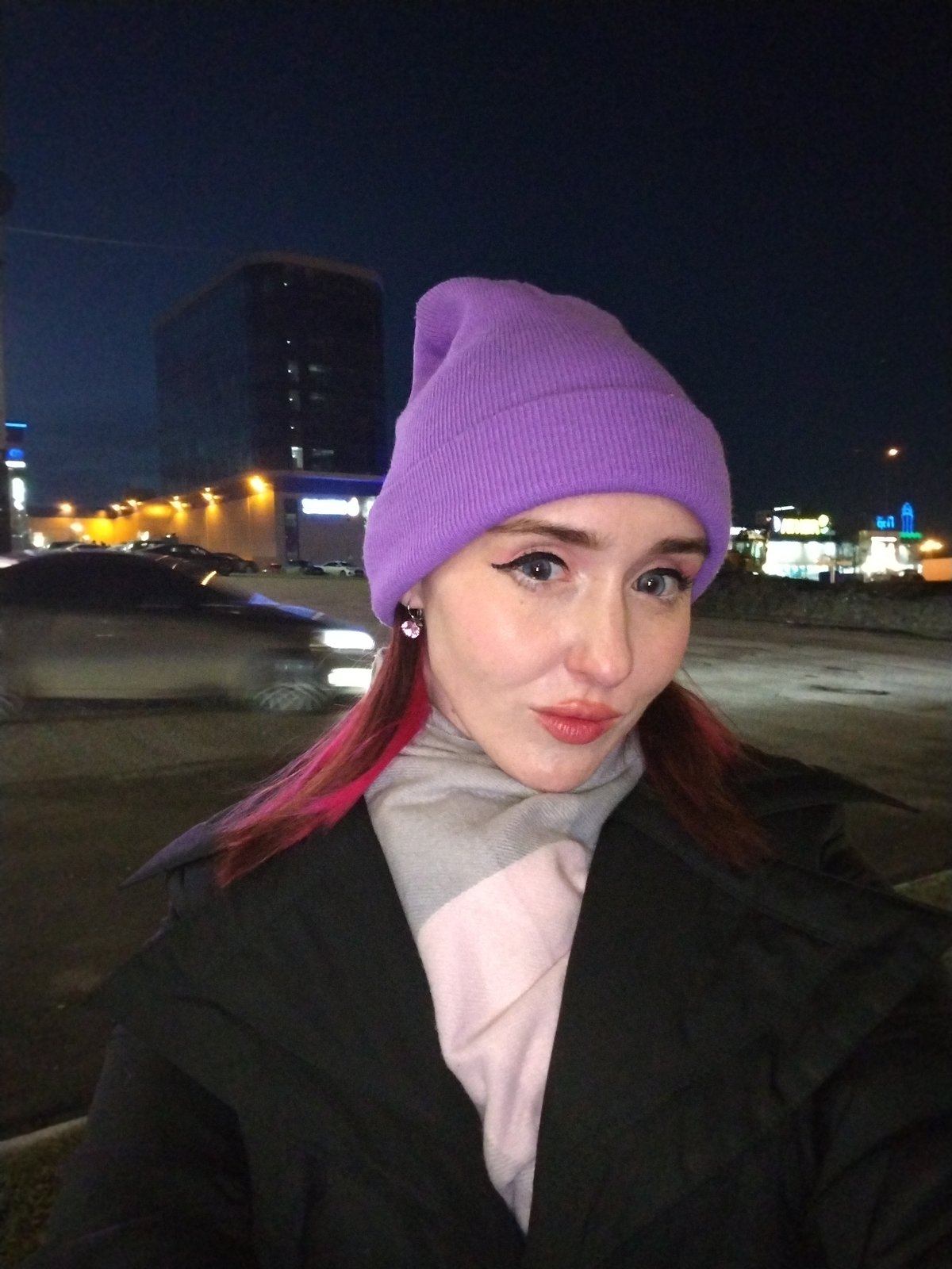 Woman in purple beanie walks through illuminated Izhevsk evening
