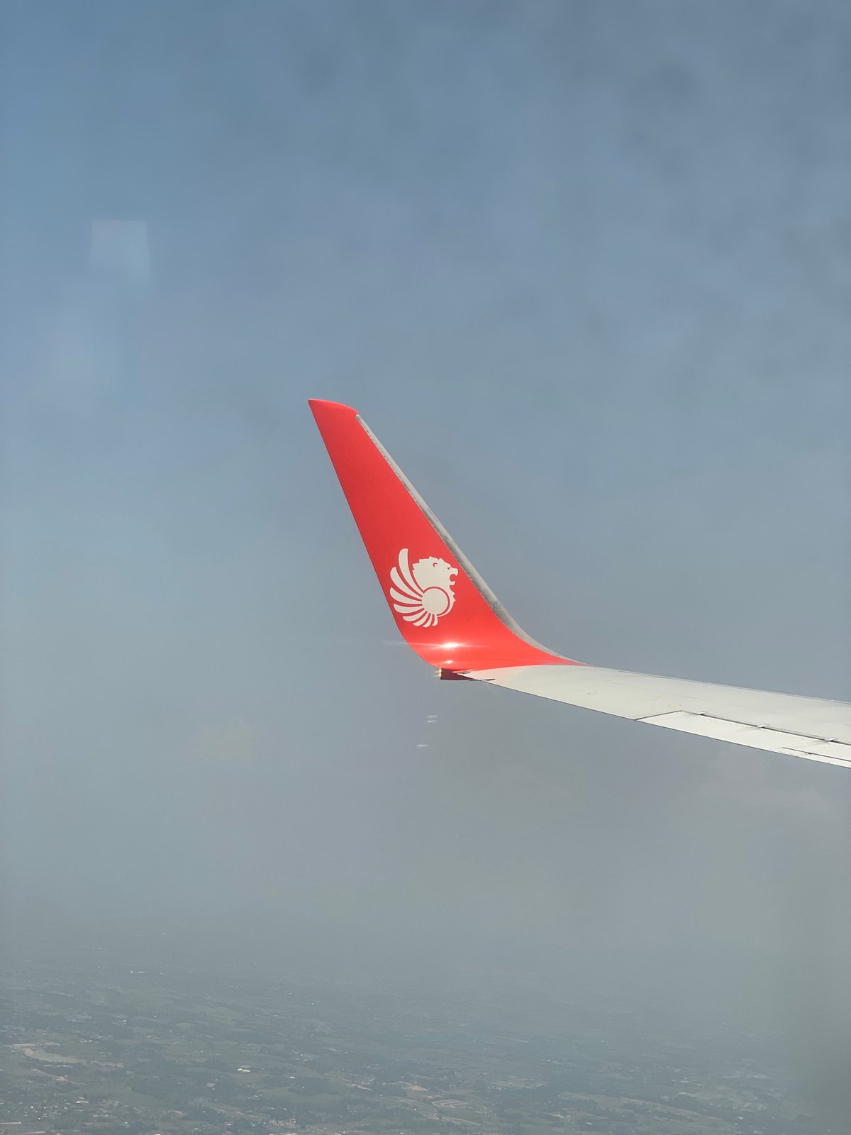 Aircraft wing photographed from airplane window over Bangkok