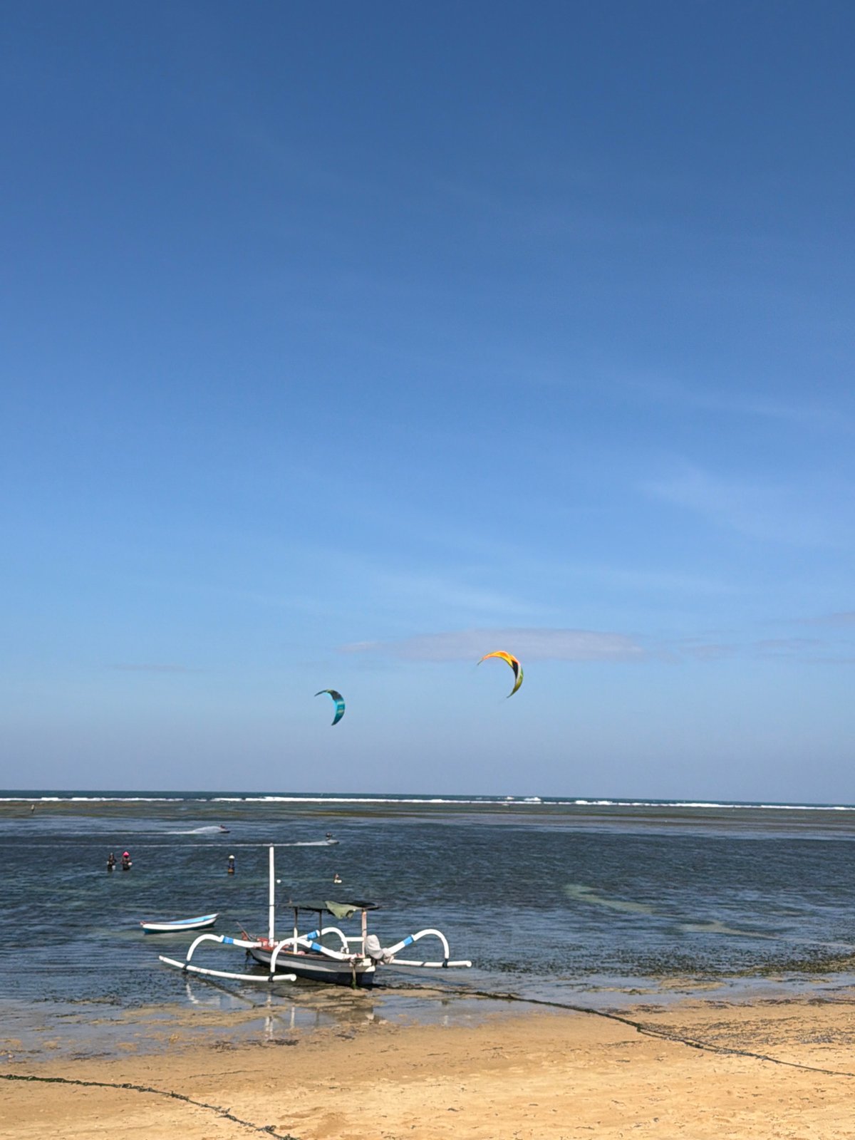 Busy morning on a Denpasar beach: kites, boats, and beachside strollers