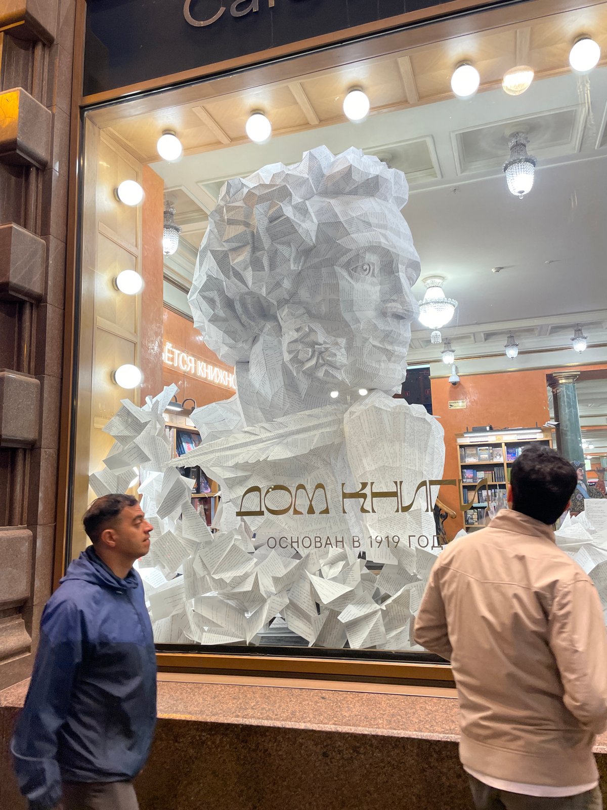 Two men browse illuminated bookstore window display at night