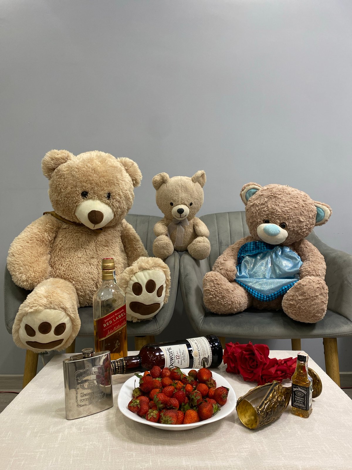 Teddy bears and whiskey bottles staged on a gray sofa