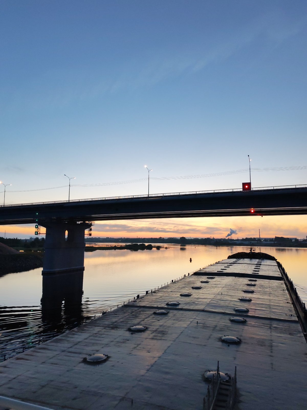 Barge passes under bridge at sunset on Sheksna River