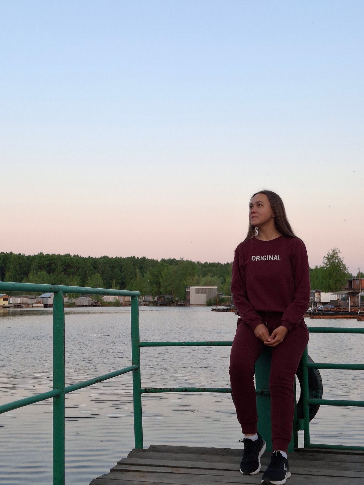 Woman sits on deck railing overlooking water in Chaikovsky