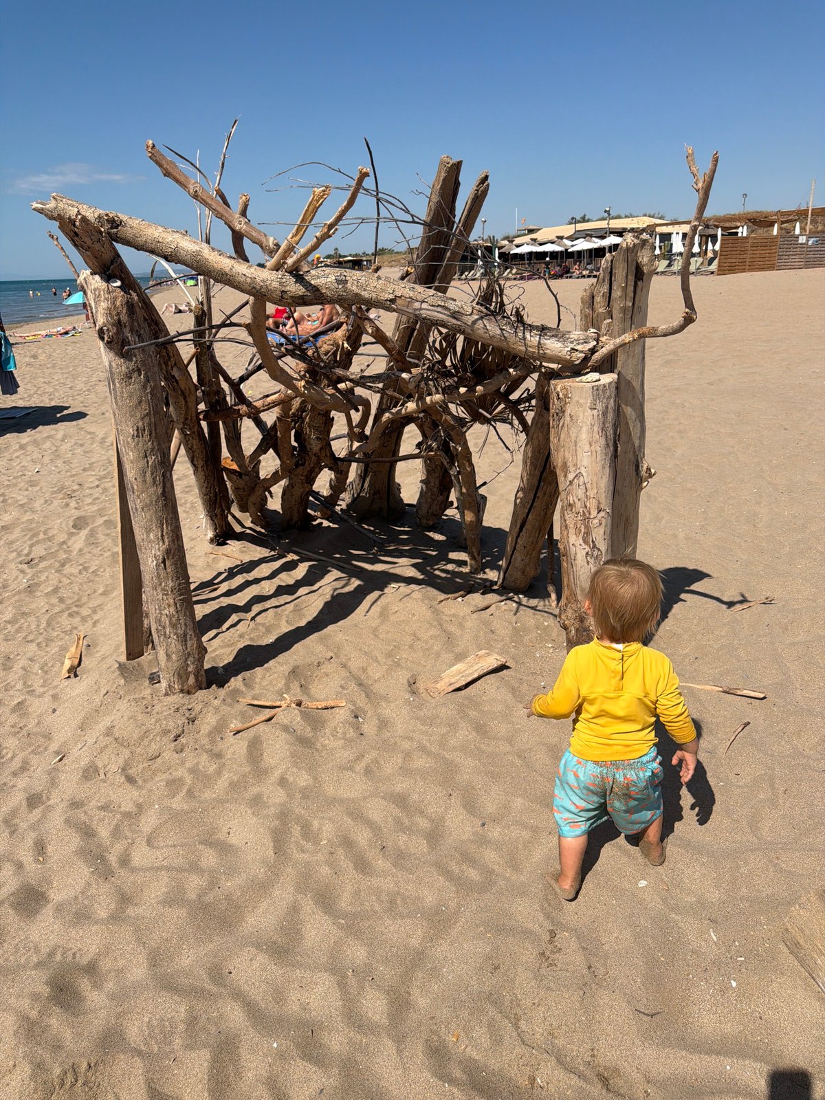 Toddler explores a sunny Sérignan beach near driftwood