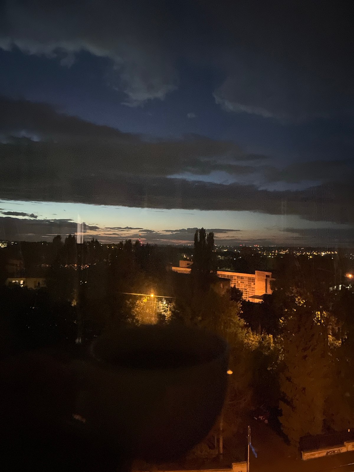 City skyline transitions from twilight to night under dramatic clouds