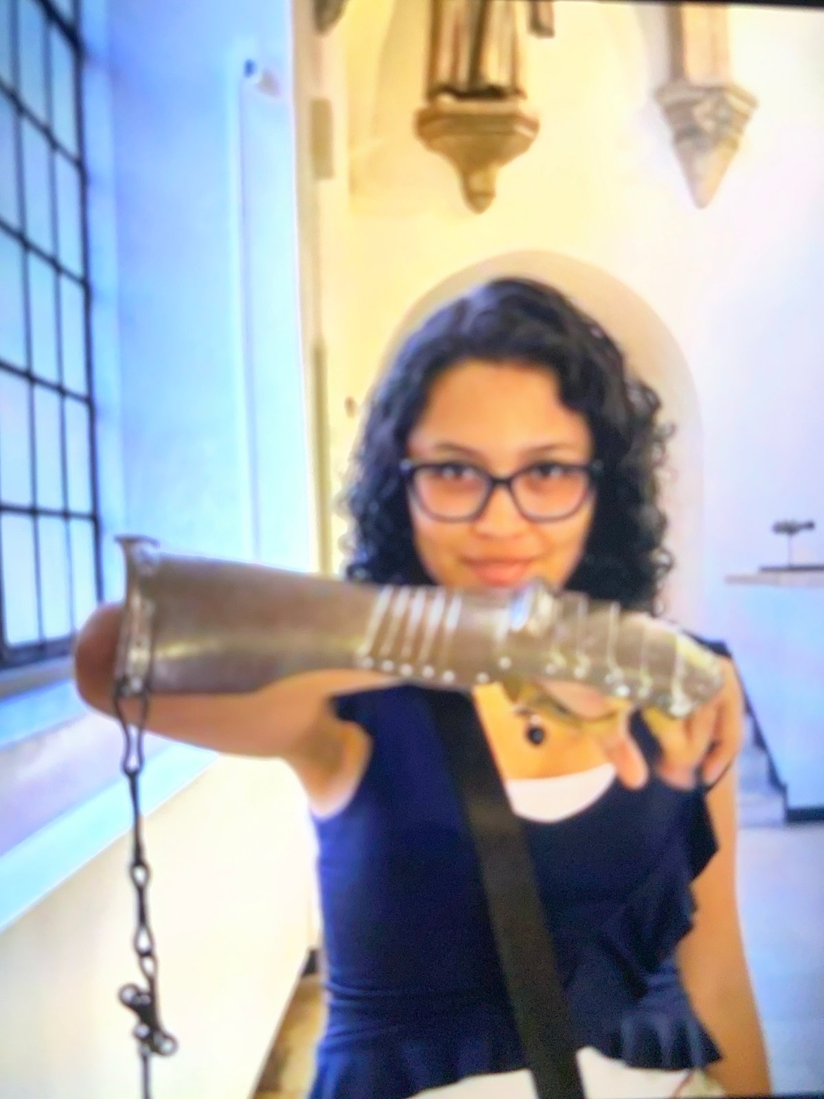 Woman examines medieval gauntlet in ornate interior setting