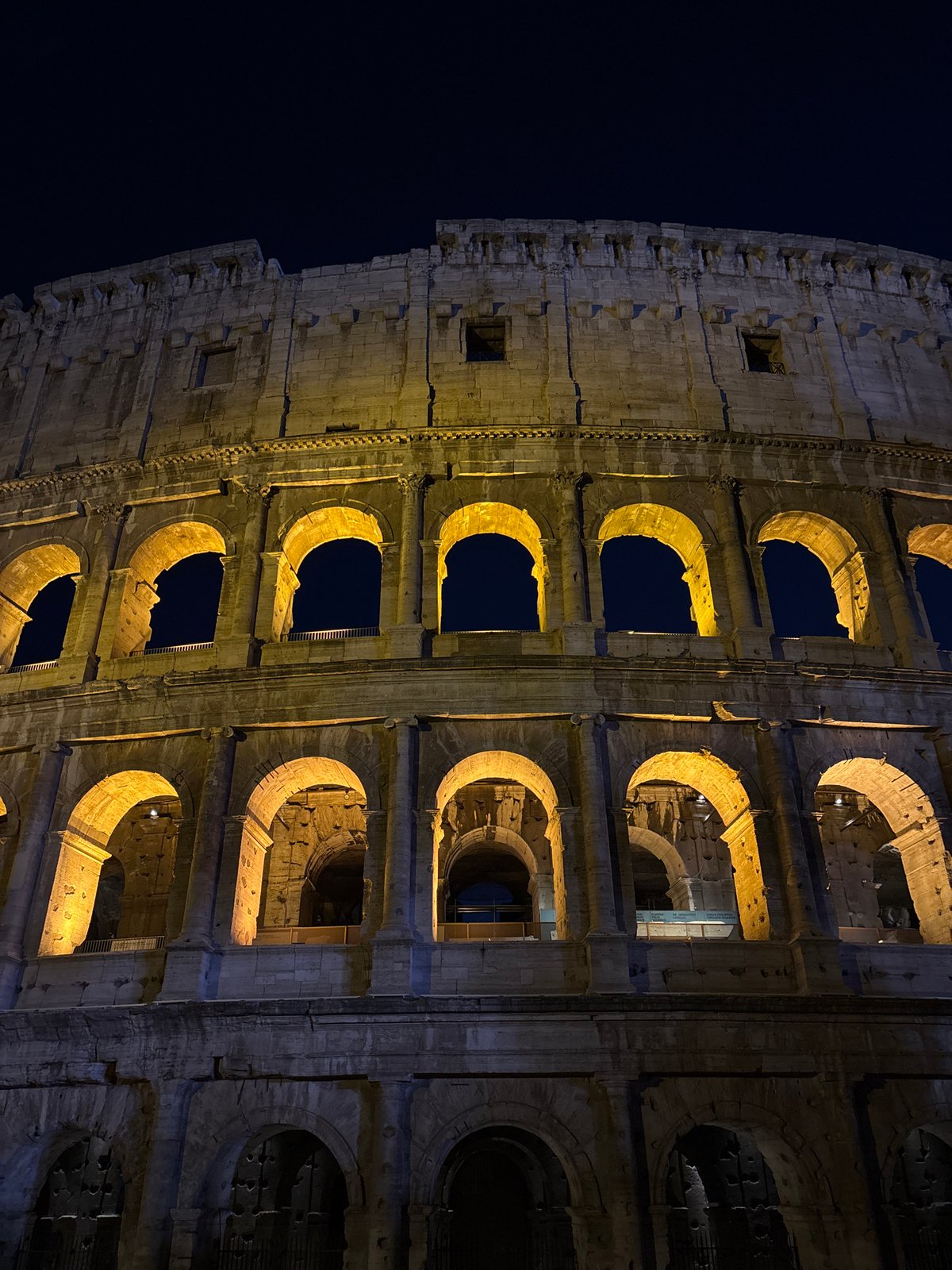 Rome's Colosseum glowing after dark, crowds outside