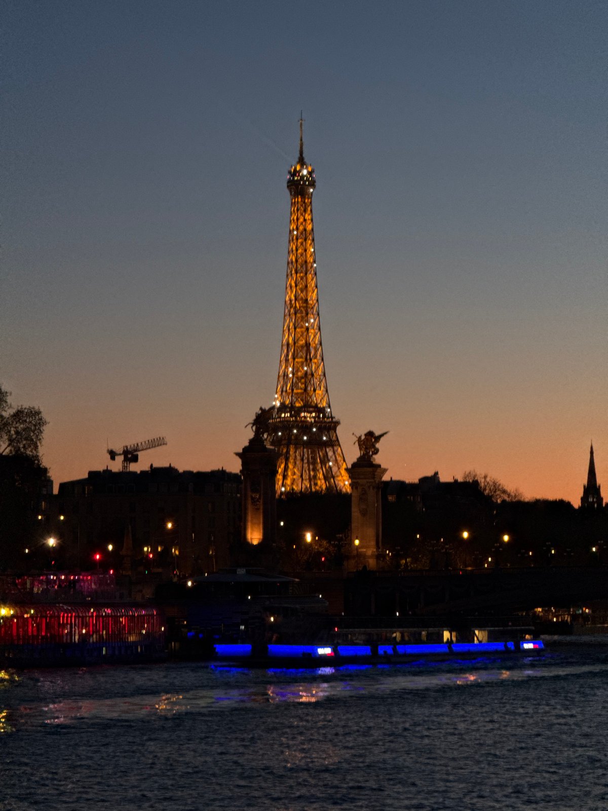 Eiffel Tower glows yellow at dusk over Seine River