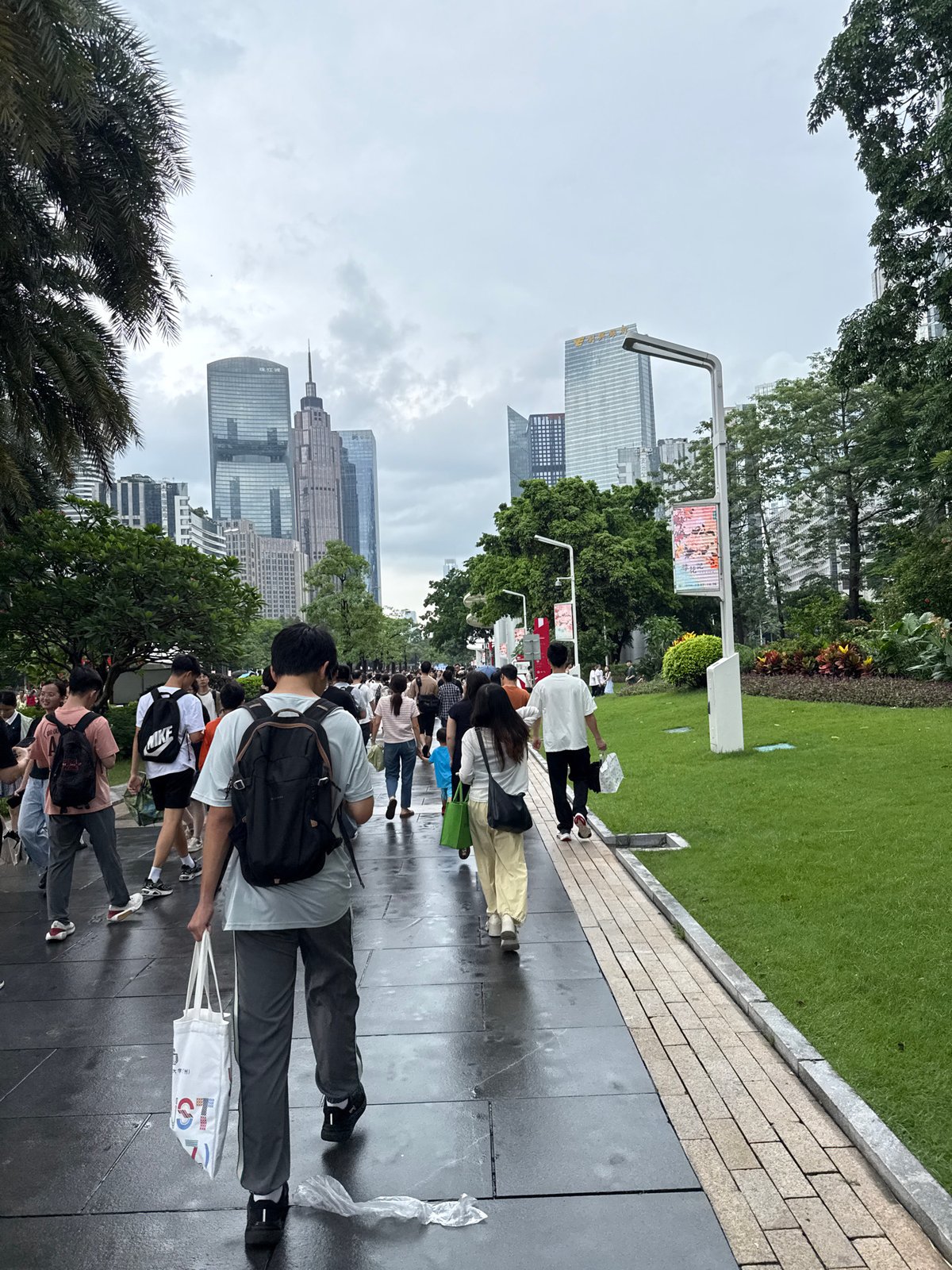 Wet plazas and crowds fill Tianhe's skyscraper district on a cloudy morning.