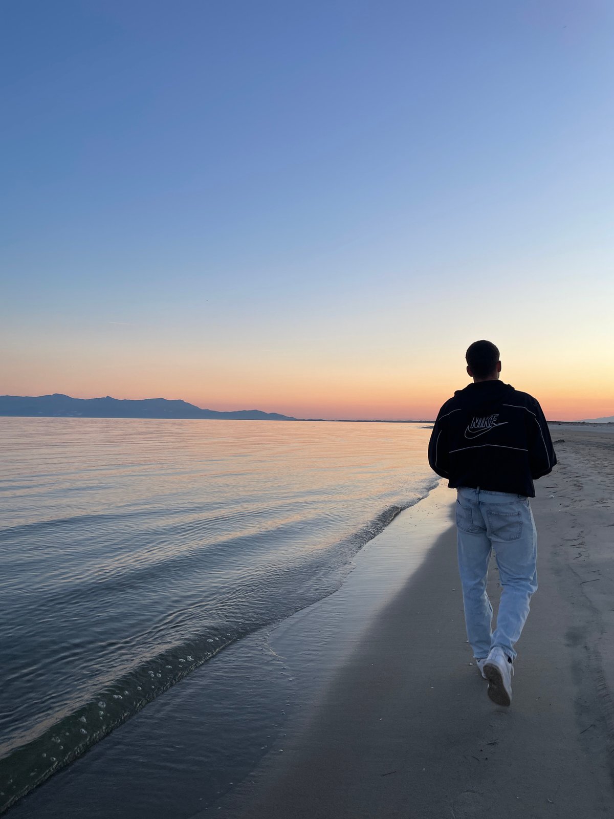 Person watches sunset on Greek beach wearing Nike jacket