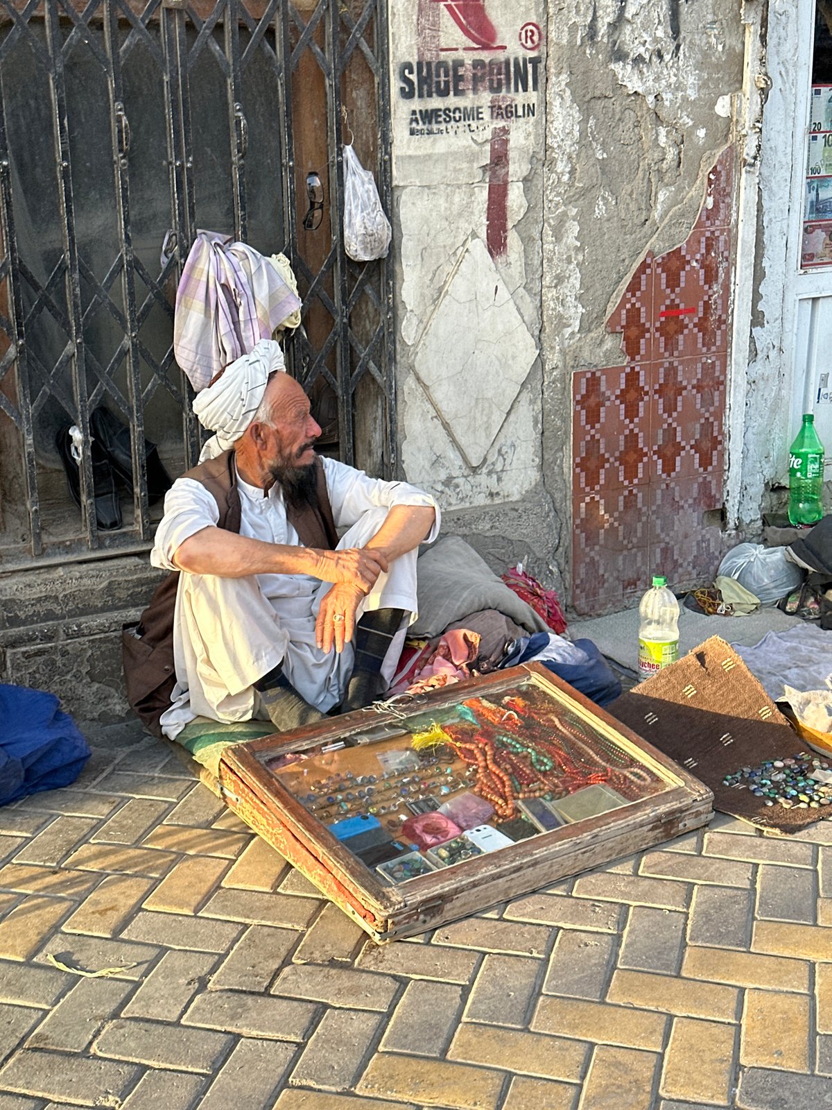 Resting against a metal grate amid belongings in Quetta