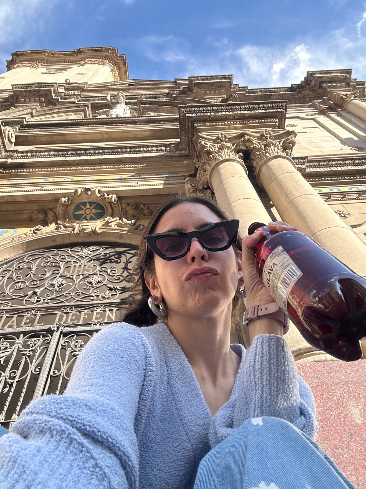 Person takes selfie with red bottle near ornate Buenos Aires building