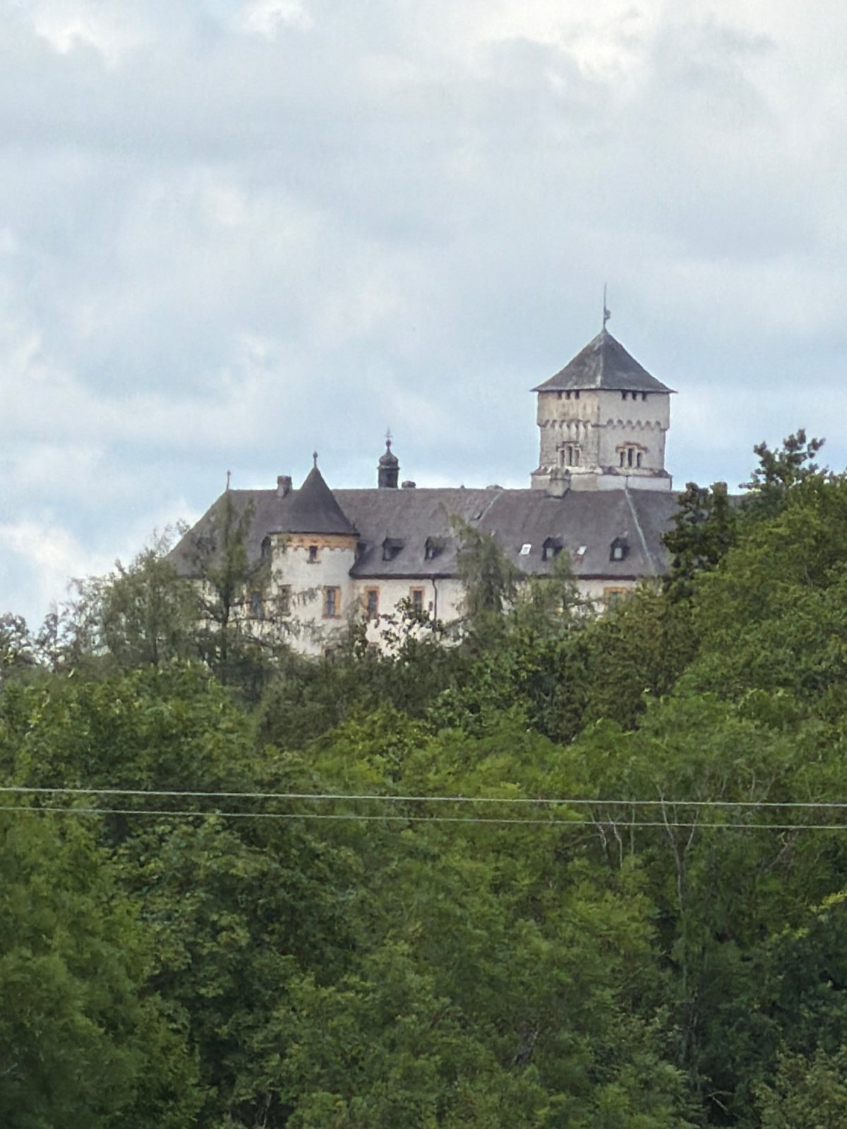 Hilltop castle peeks through summer trees in northern Bavaria