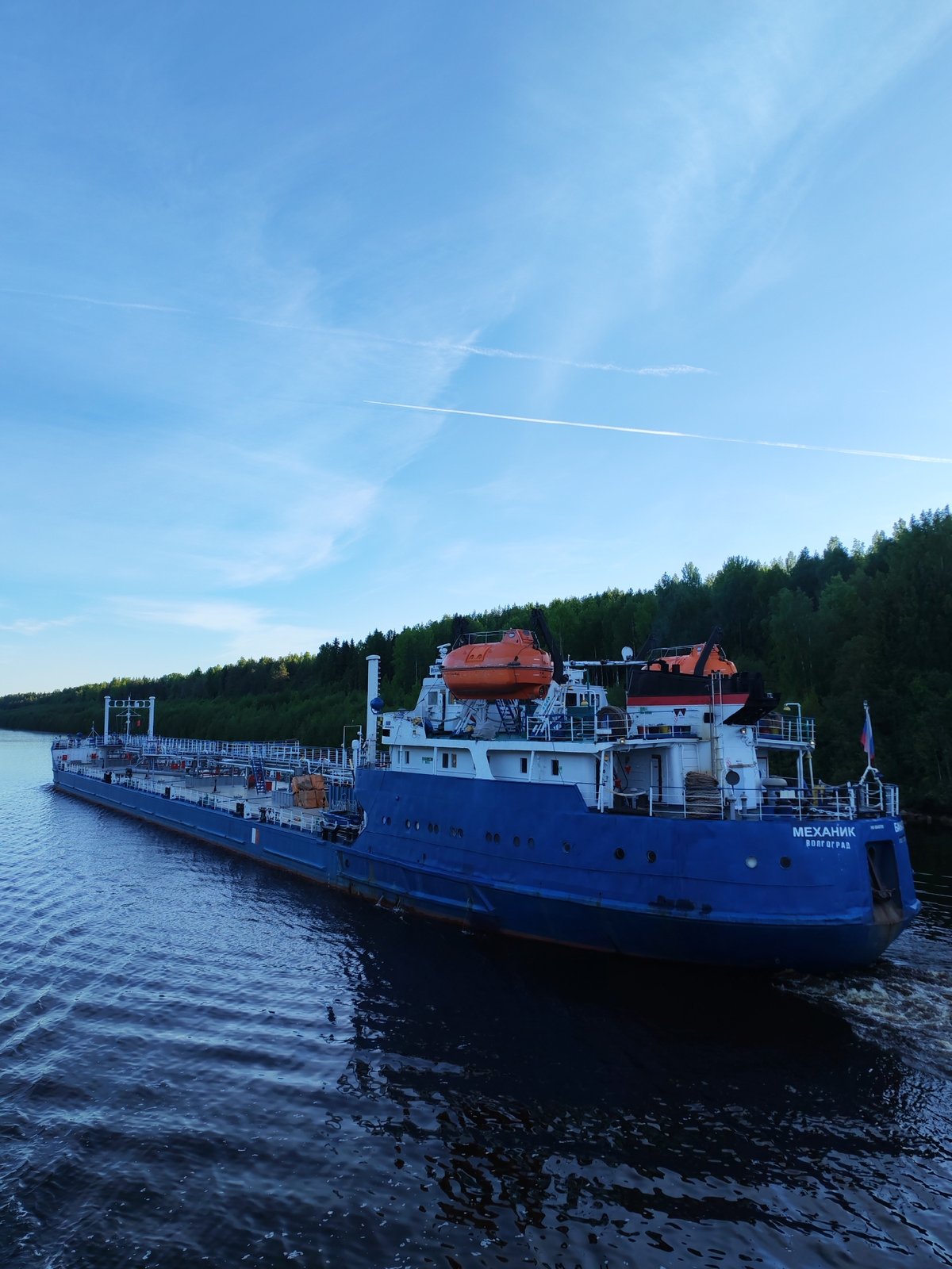 Blue tanker МЕХАНИК БАНАТОВ navigates Russian waterway near forests