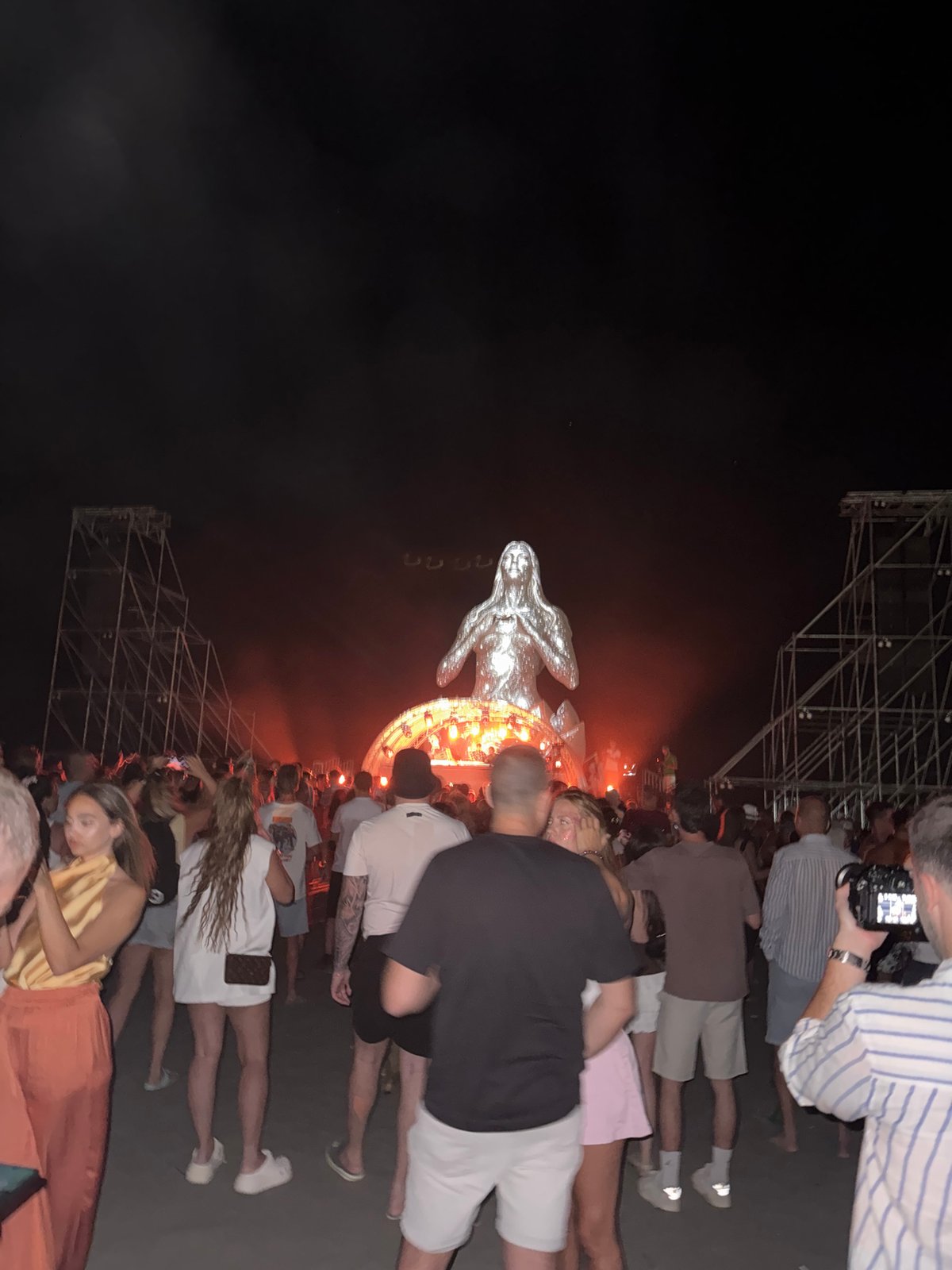 Night crowd gathers around glowing metallic statue at outdoor event