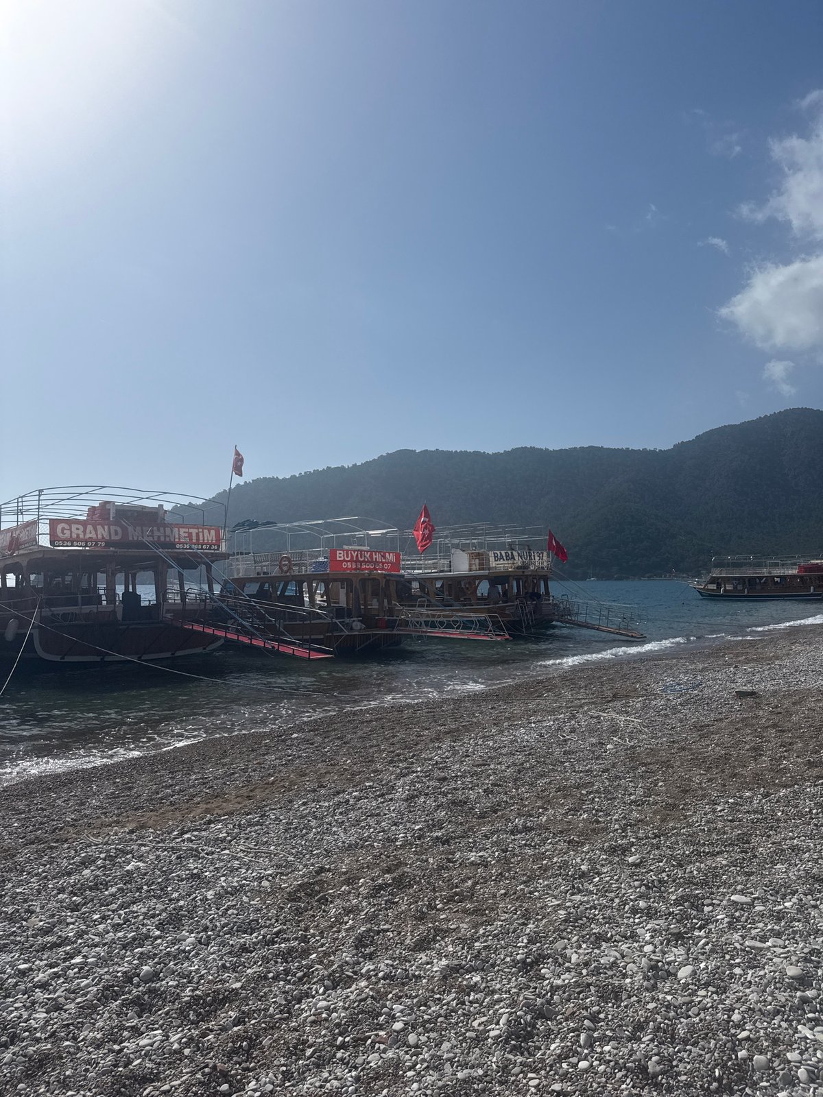 Tour boats dock at Kumluca beach as morning visitors gather