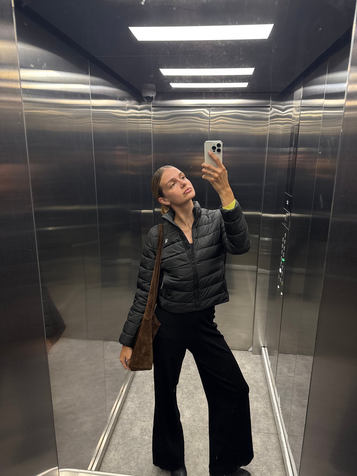 Woman takes selfie in elevator wearing black outfit