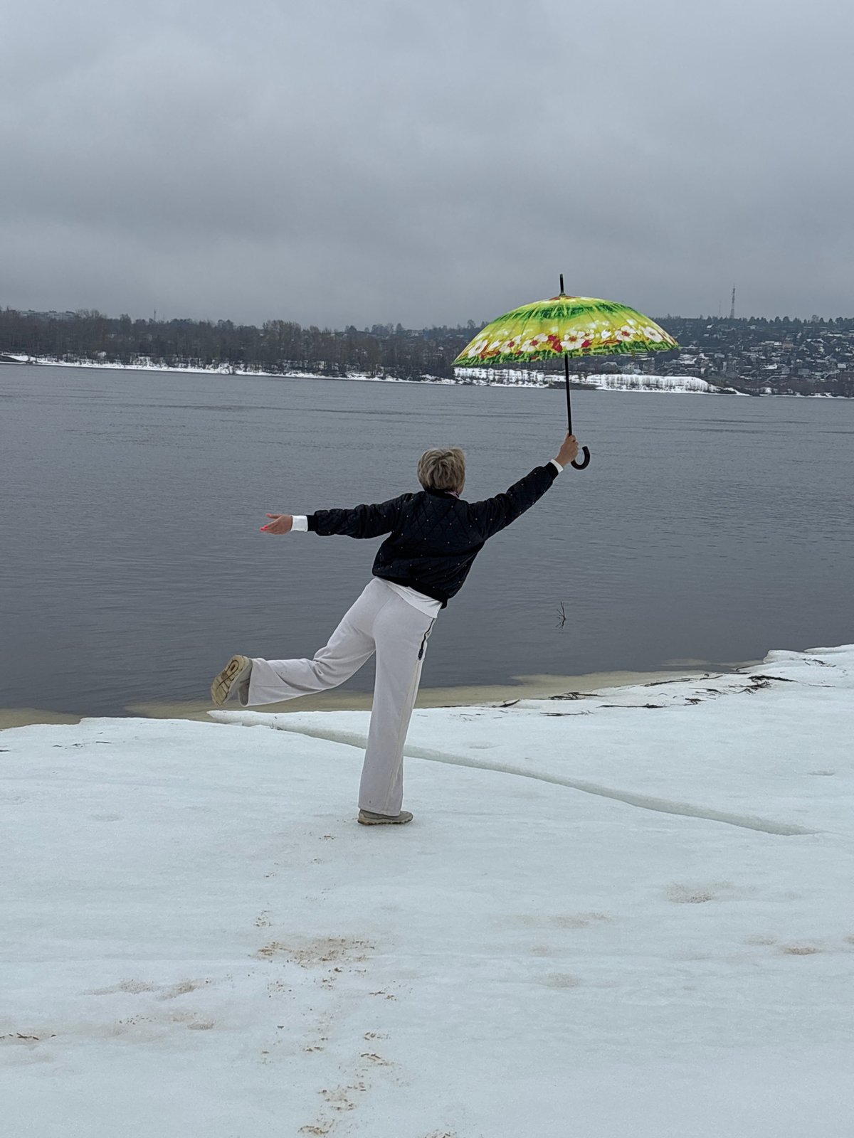 Woman gestures toward water on snowy shore in Chaikovsky