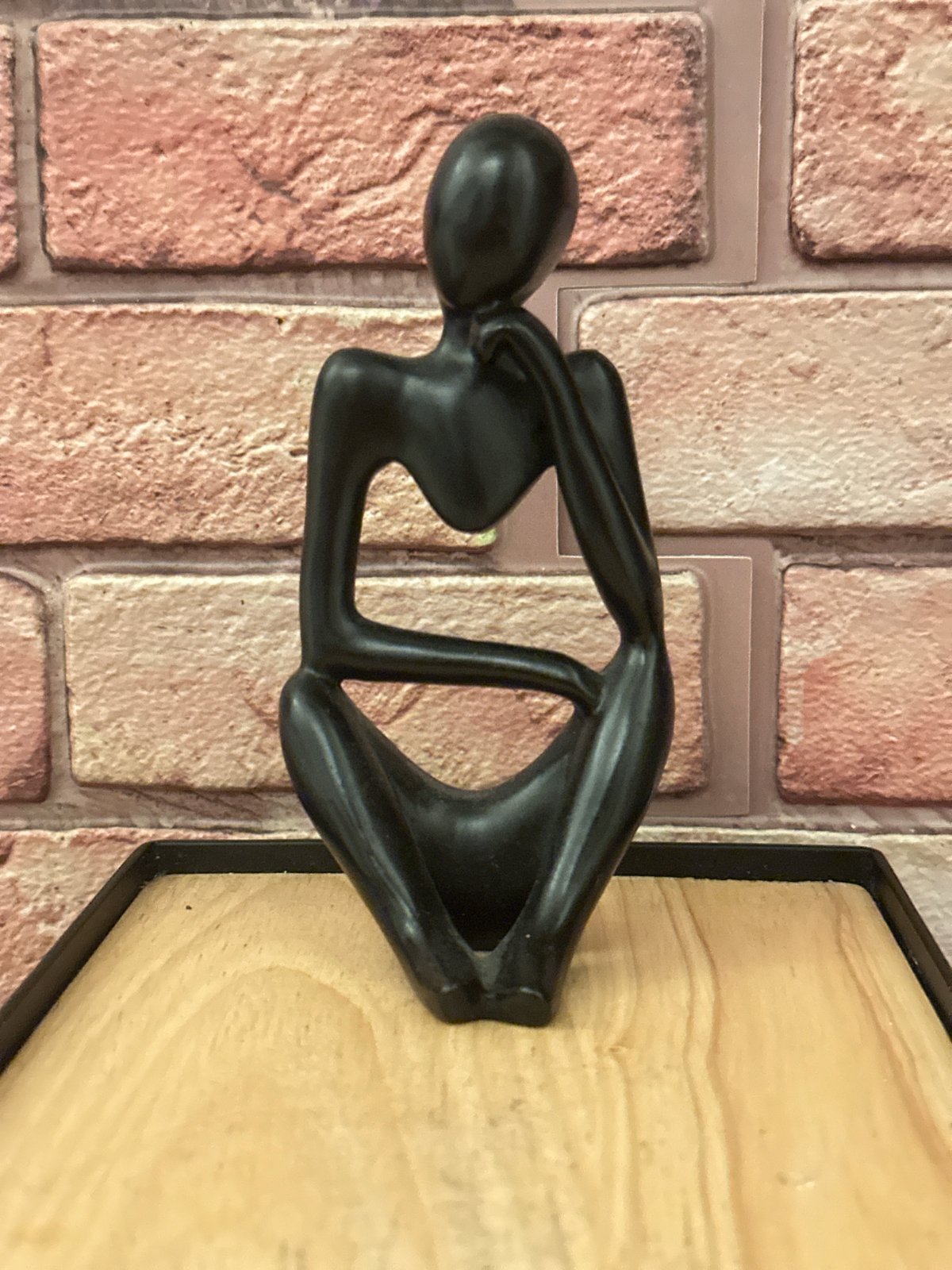 Black contemplative sculpture observed on London brick wall display