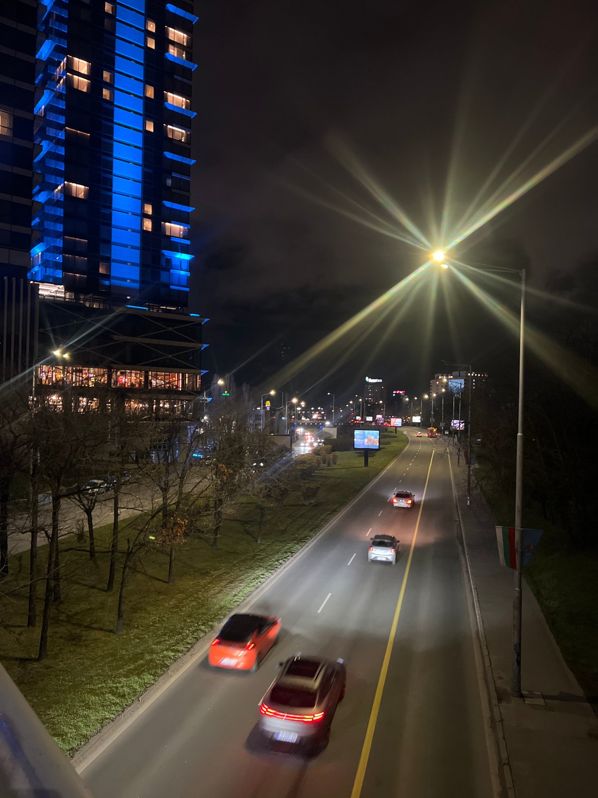 Evening traffic flows past blue-lit buildings in Sofia