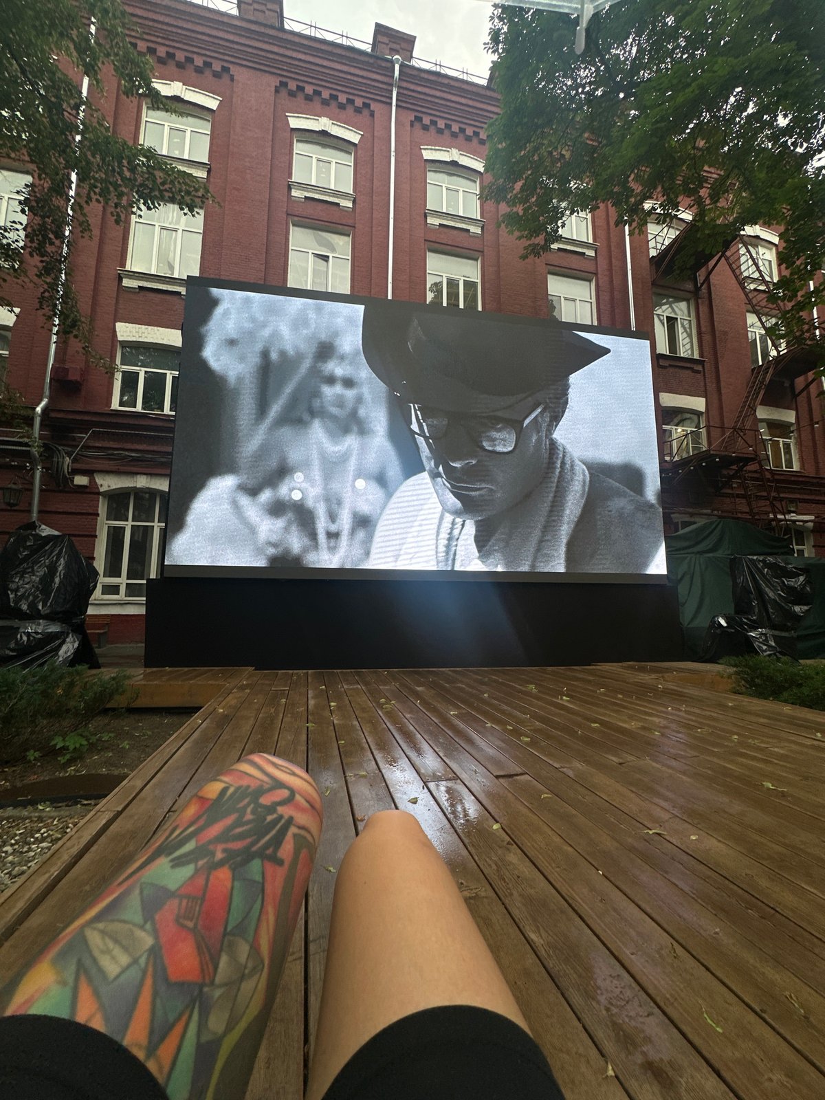 Outdoor screen and tattooed leg on a Moscow wooden deck