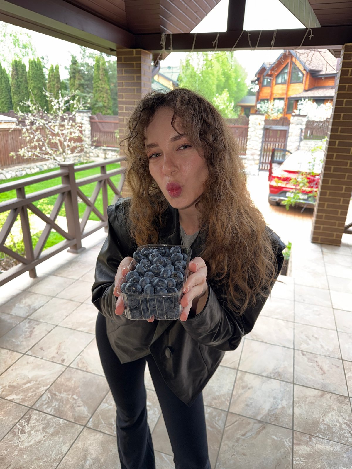 Woman holds blueberry container on porch in Новоглаголево