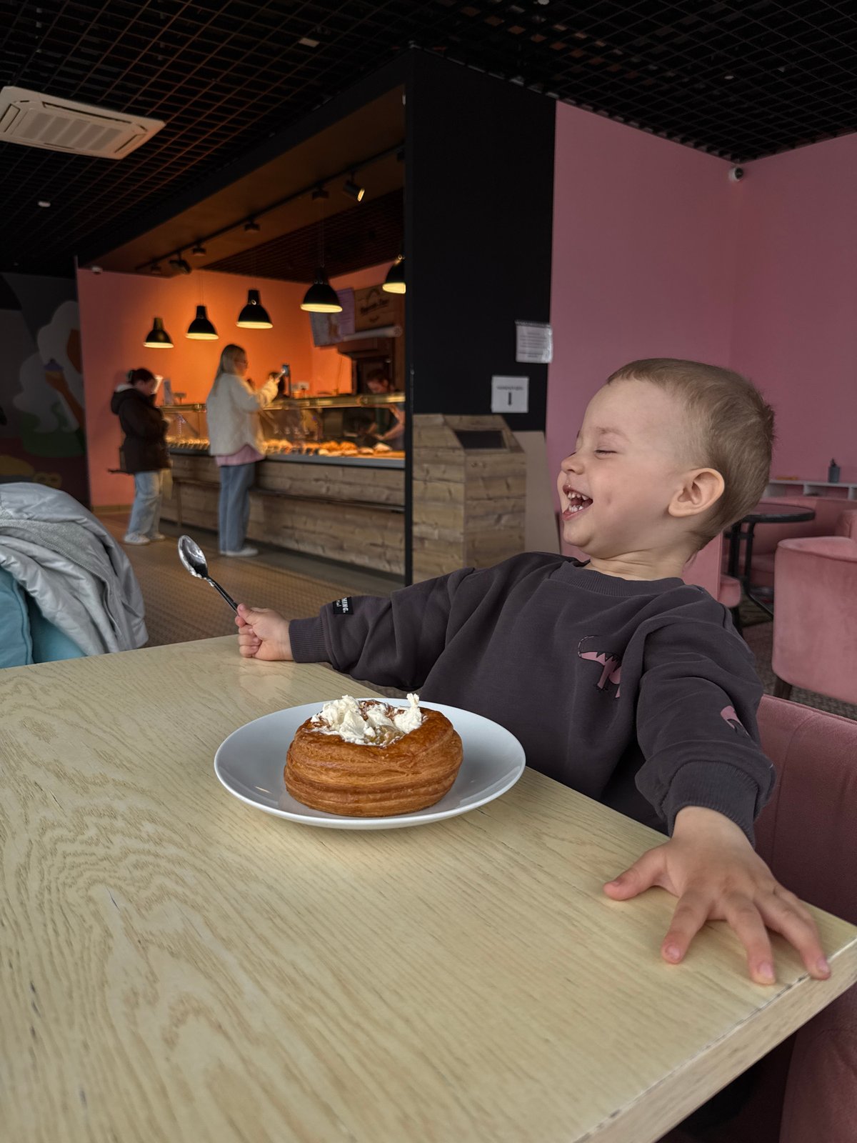 Child enjoys cream pastry at table, laughing with delight