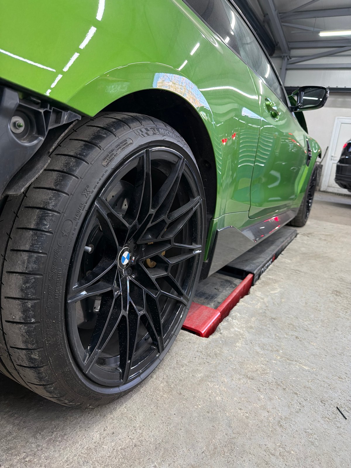 Green BMW M4 undergoing repair work in workshop